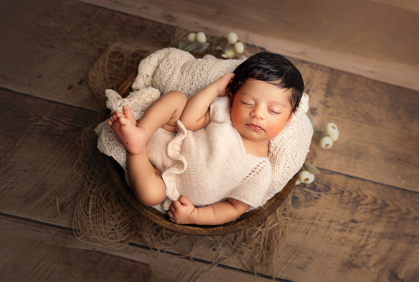 Sleeping newborn baby wrapped in soft beige fabric lying in wooden bowl on rustic wooden surface at Bothell