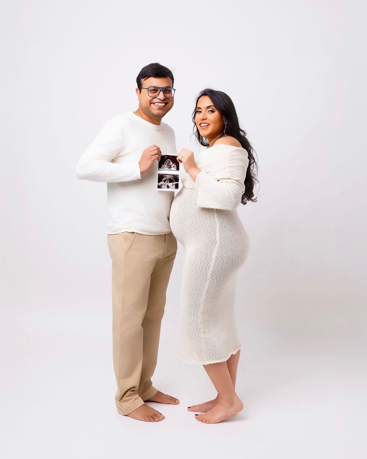 A couple in white outfits poses together for a series of pregnancy announcement photos against a light background at bothell