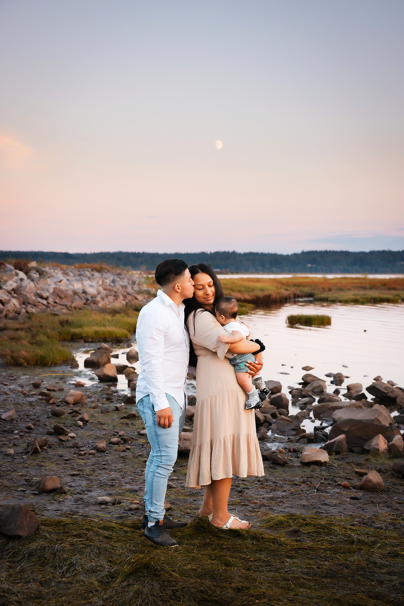 A couple shares a romantic moment at sunset on a rocky beach with seagulls in the background.