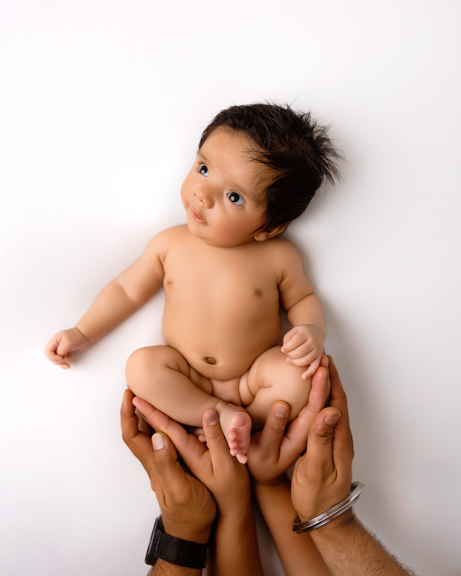 Minimalist newborn photography with baby on white background showing tiny hands and feet.