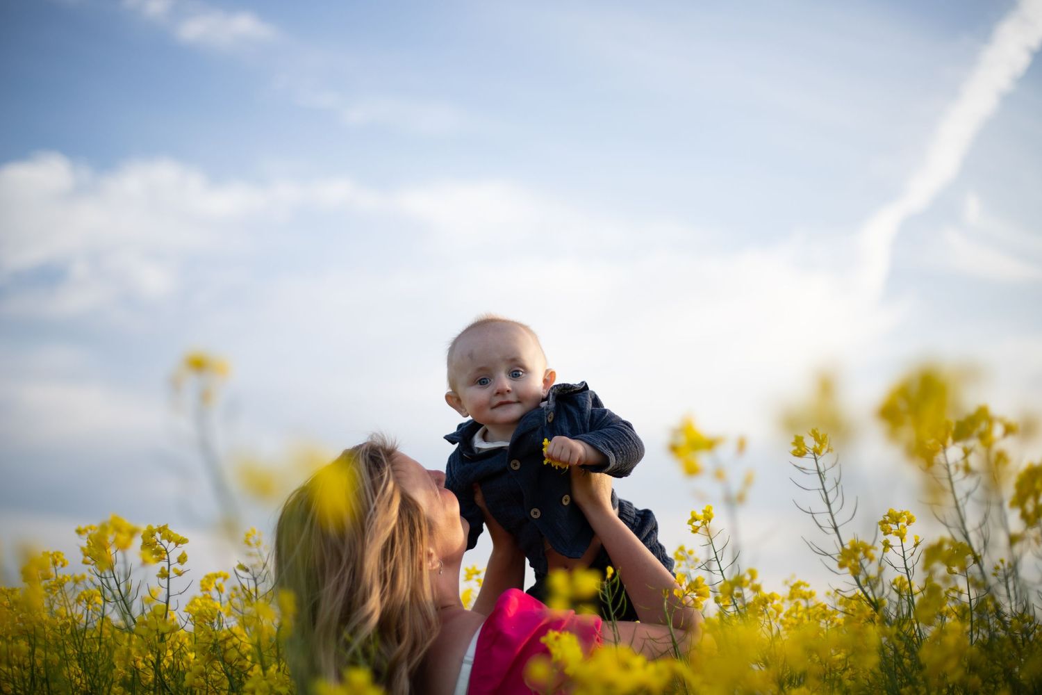 I ett rapsfält står en mamma som lyfter upp sin son mot himlen.