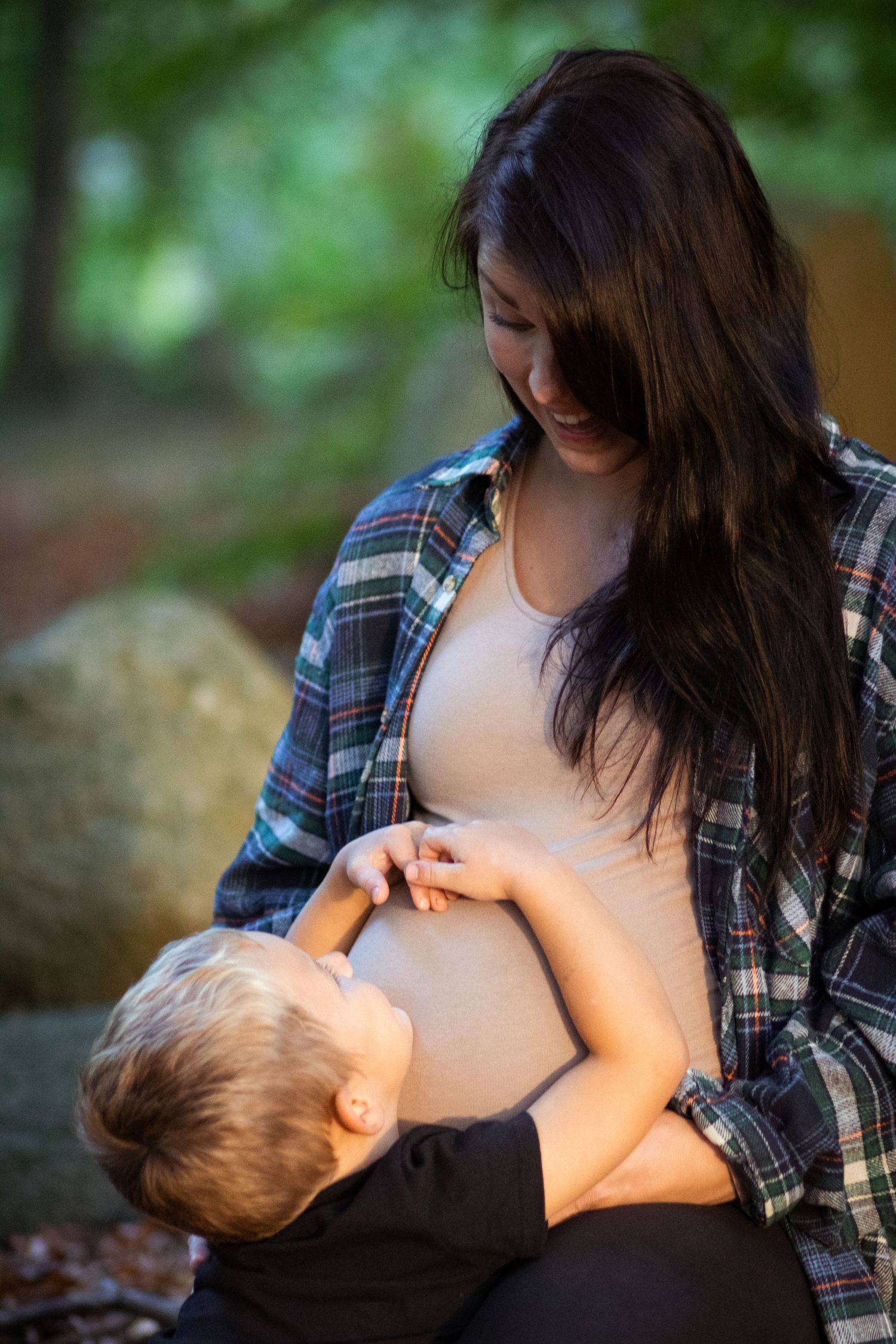 En gravid mamma sitter och tittar ner på sin son som har omfamnat hennes gravida mage.