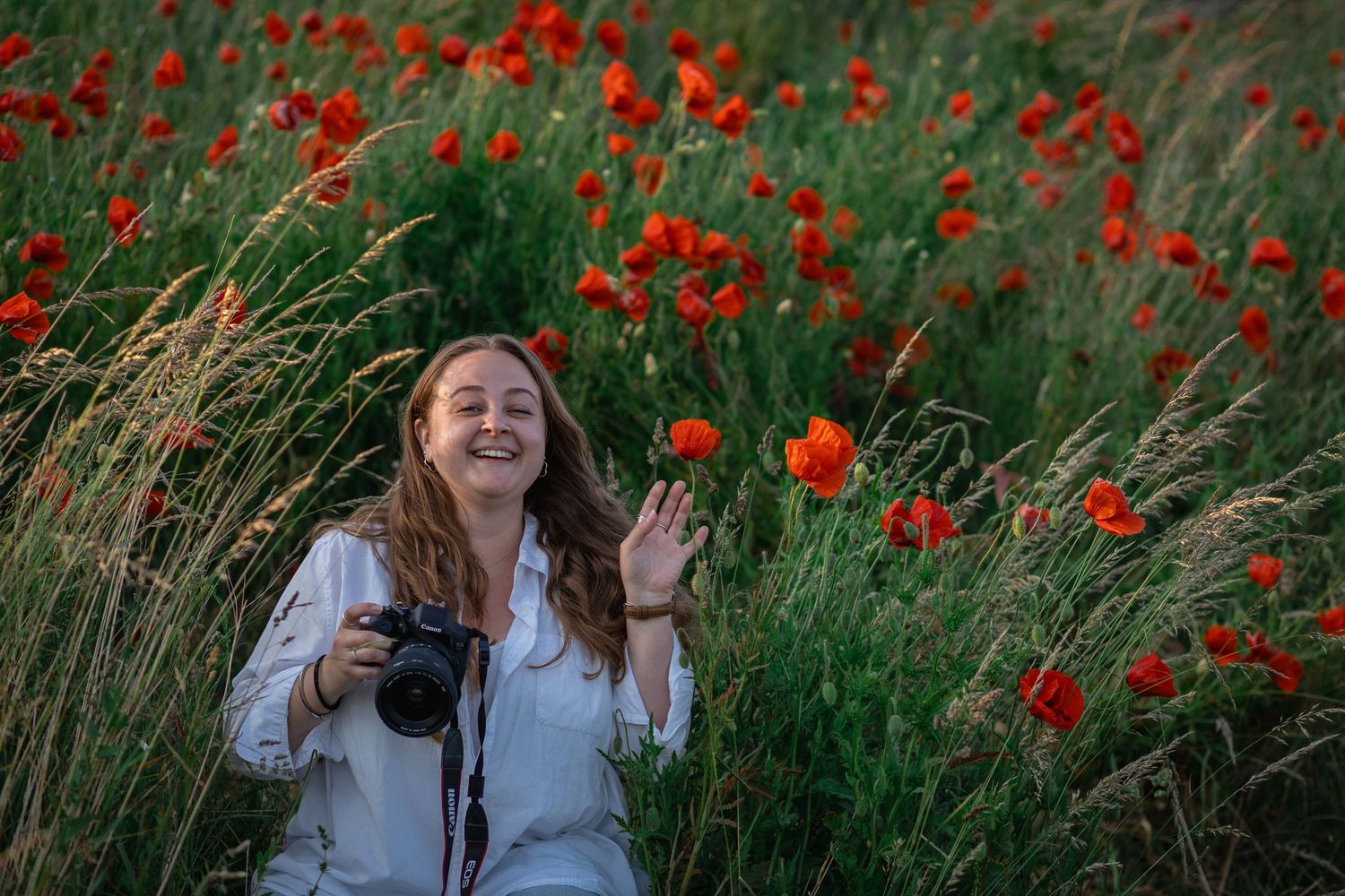 Kvinnlig fotograf i fält med röda vallmoblommor, med kameran redo i handen.