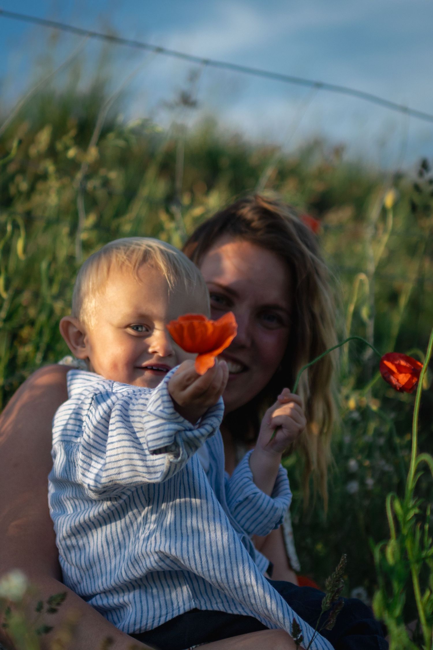 I ett vallmofält sitter en mamma och hennes son som visar upp en vallmoblomma.