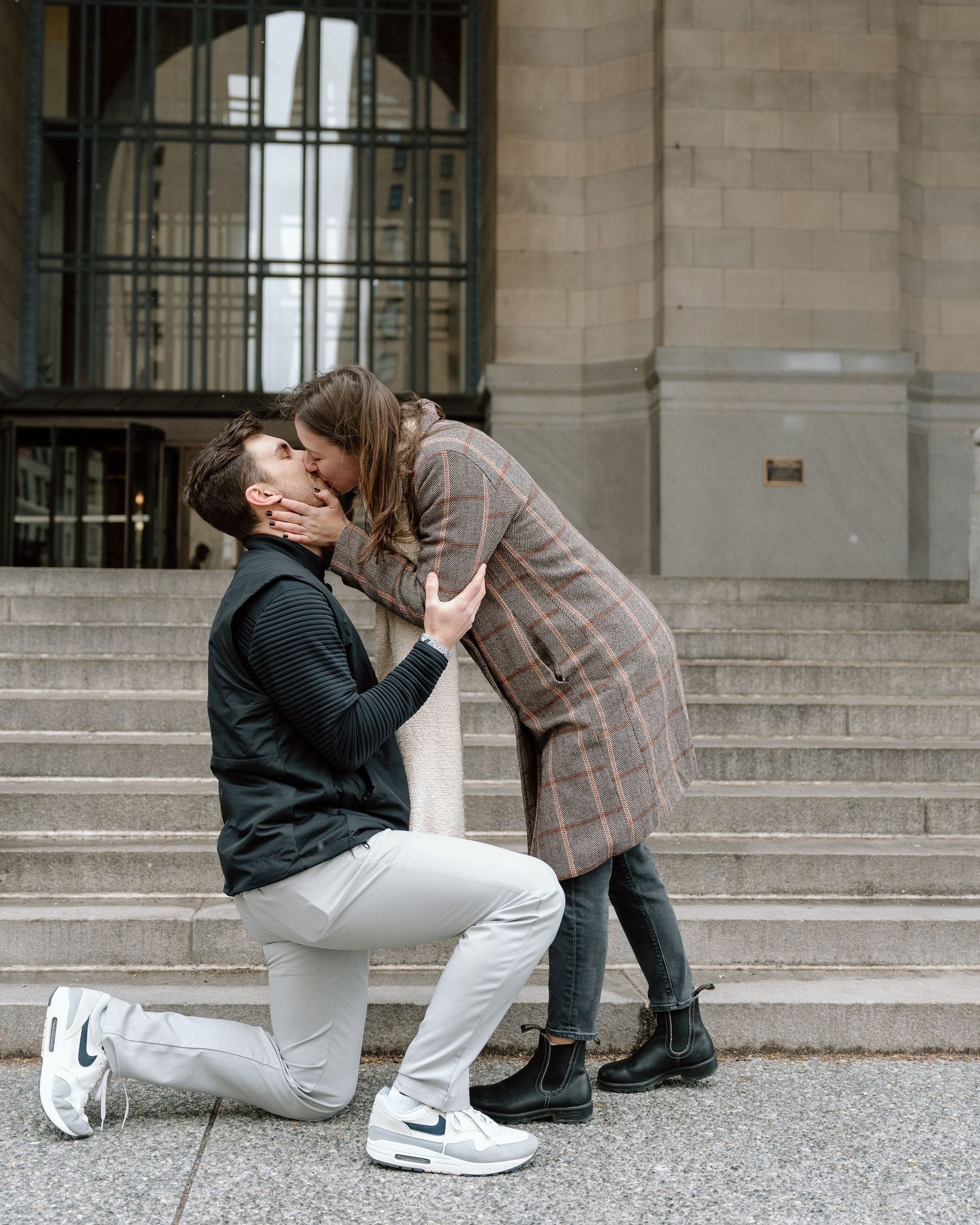 A romantic proposal moment captured on stone steps outside a building.