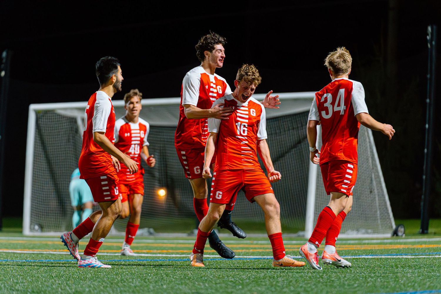 Soccer players in red and white uniforms celebrating together on an illuminated field at night.
