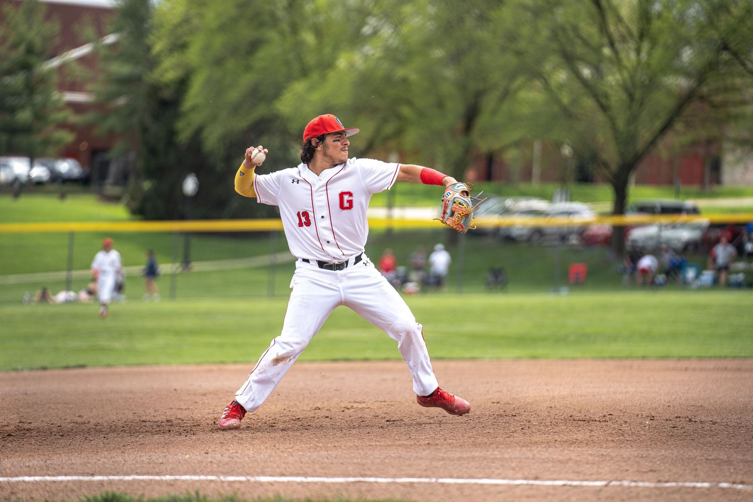 Baseball pitcher in white uniform mid-delivery on third base during game.