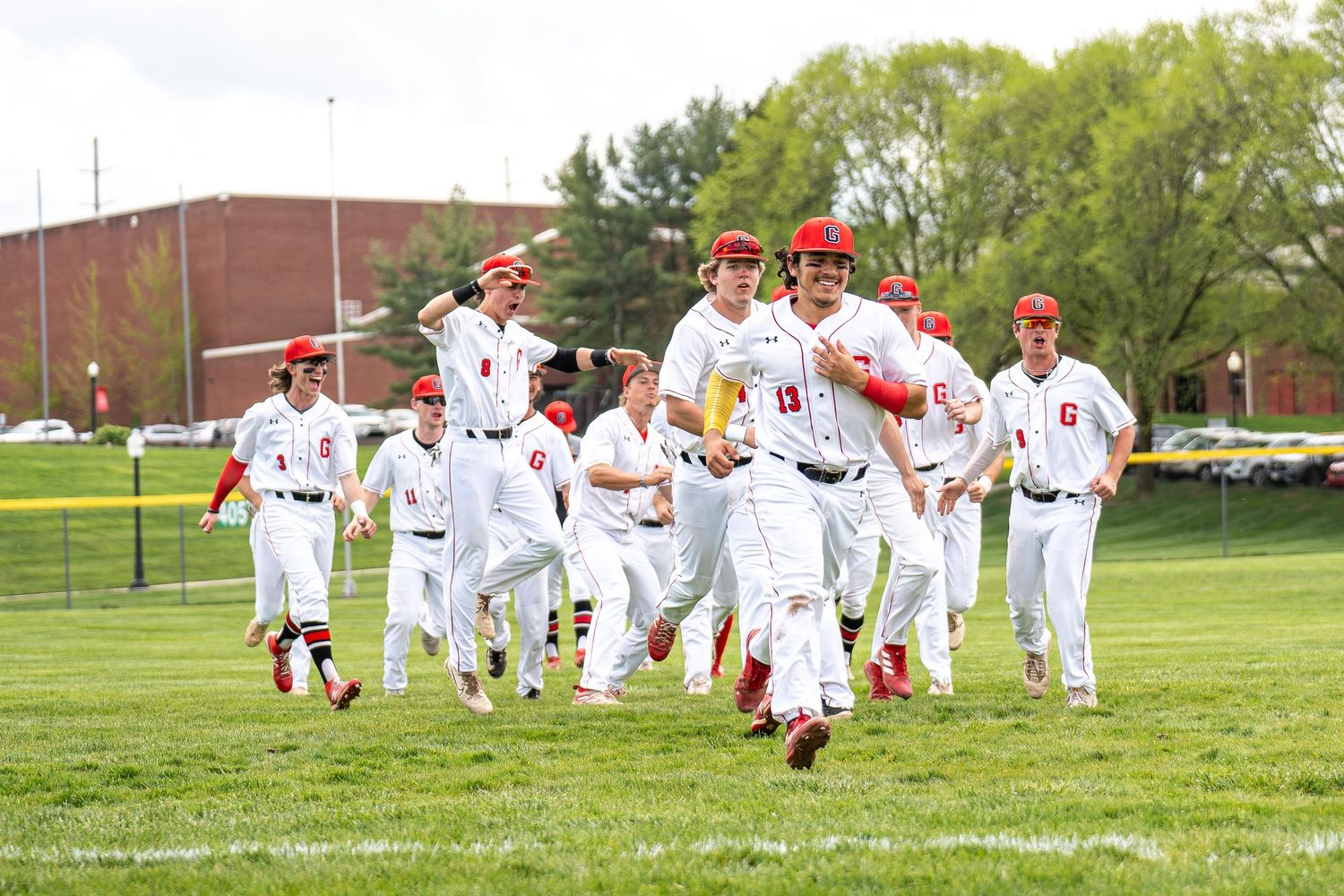 Baseball team in white uniforms celebrating victory on green field.