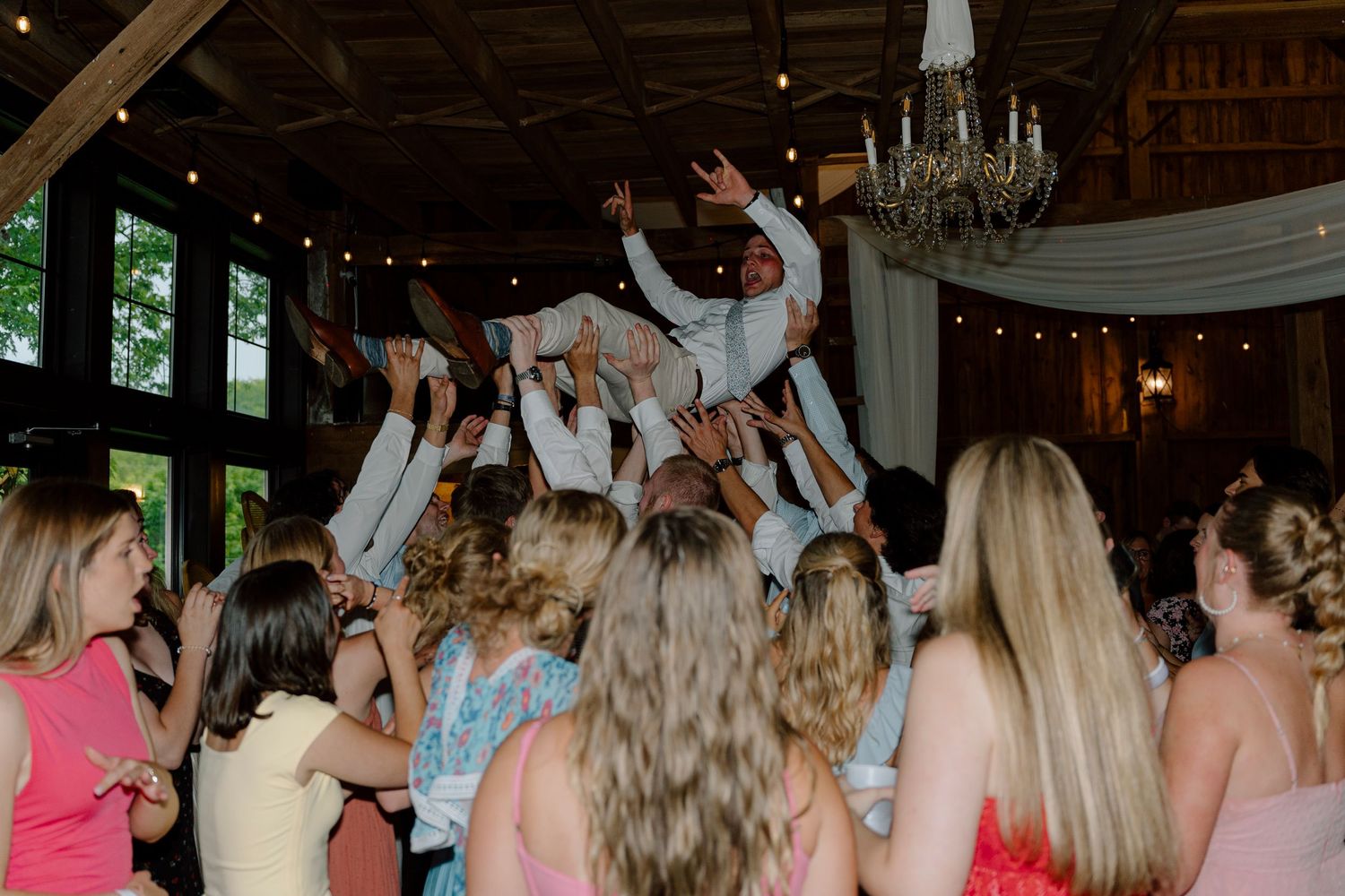 Wedding guests lift and celebrate on dance floor during reception party.