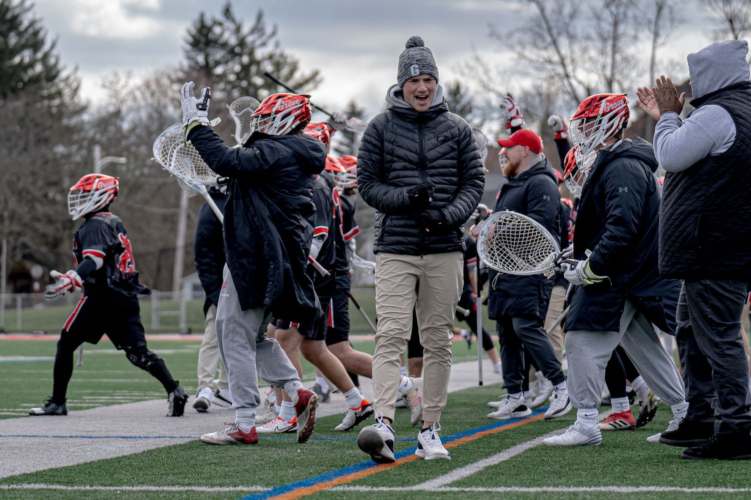 Grove City College Men's Lacrosse team members and coaches gathering on sideline during cold weather game