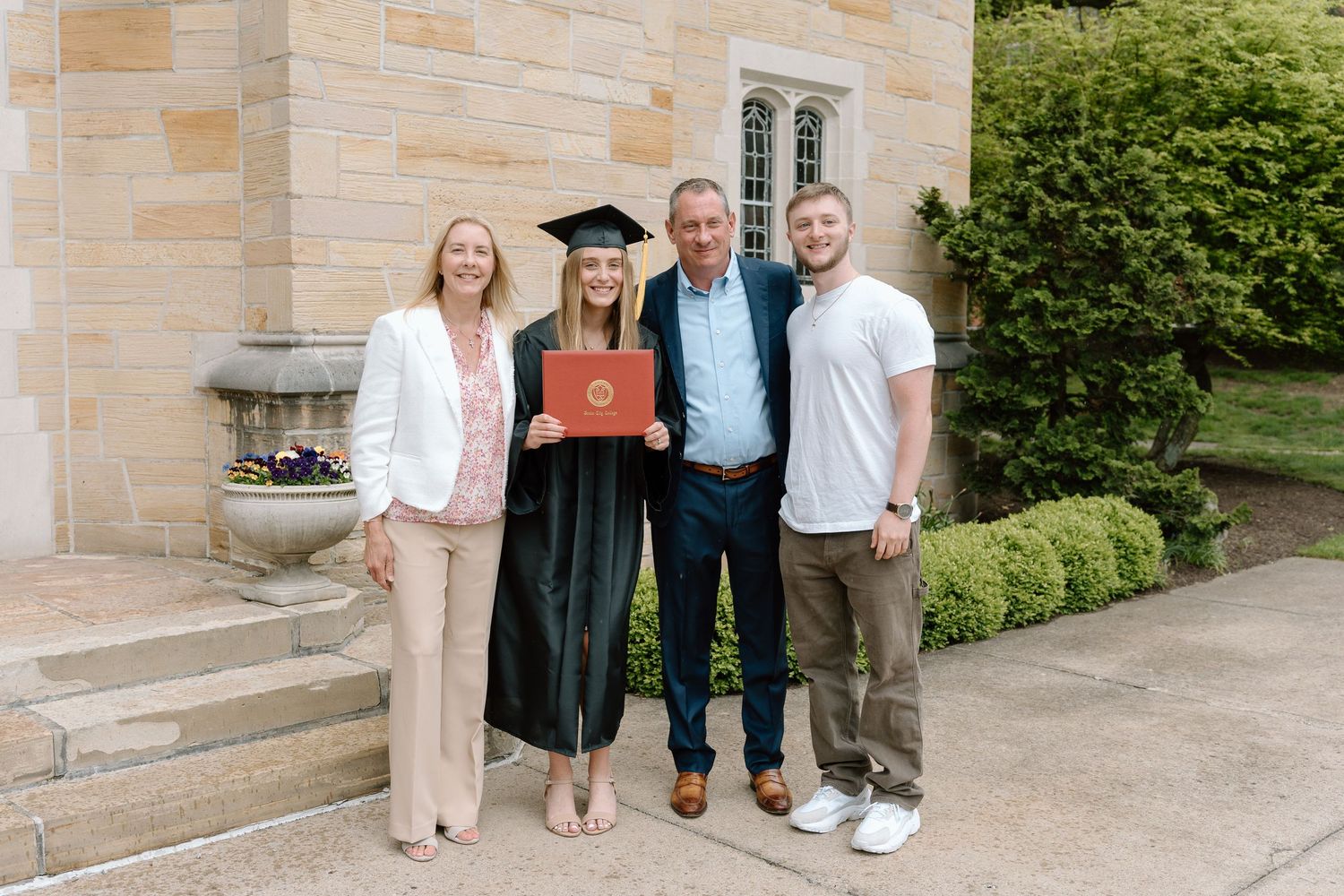 Family graduation photos taken outside stone building with landscaped grounds.