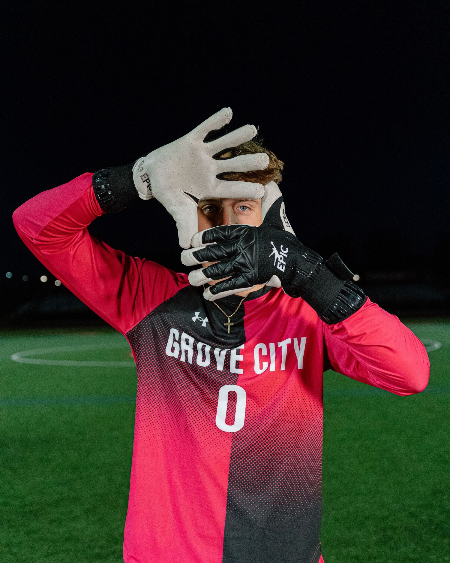 Soccer goalie in red jersey and black gloves gestures during a nighttime match on illuminated field.