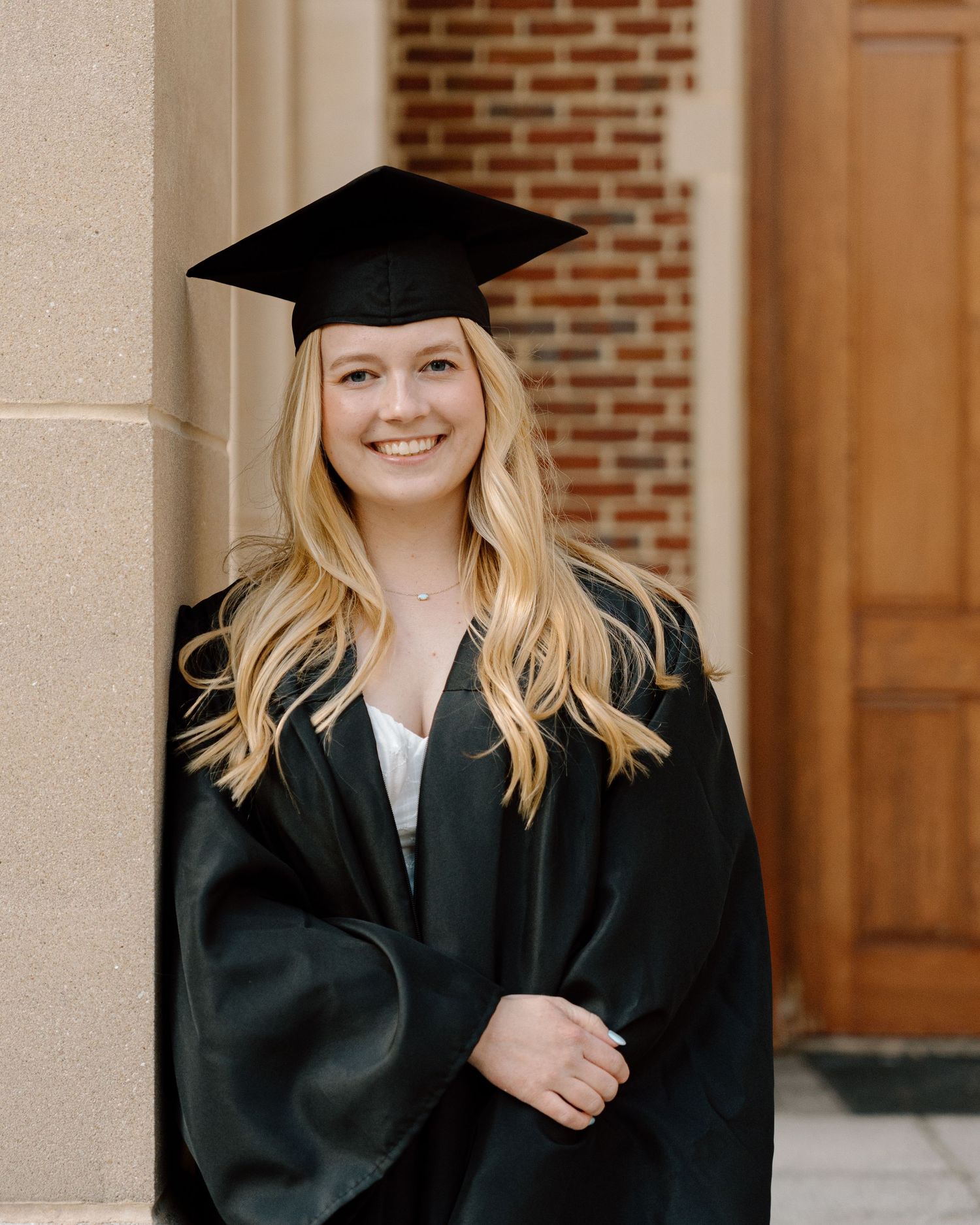 Graduation portrait series of student in cap and gown against brick building.