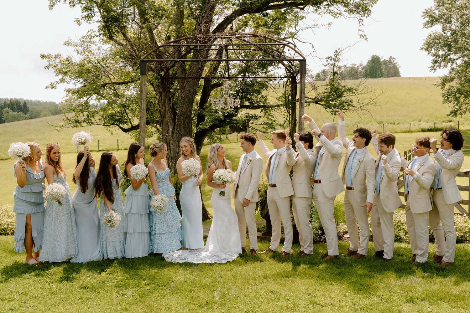 Wedding party lined up in light blue and khaki attire outdoors in natural setting.