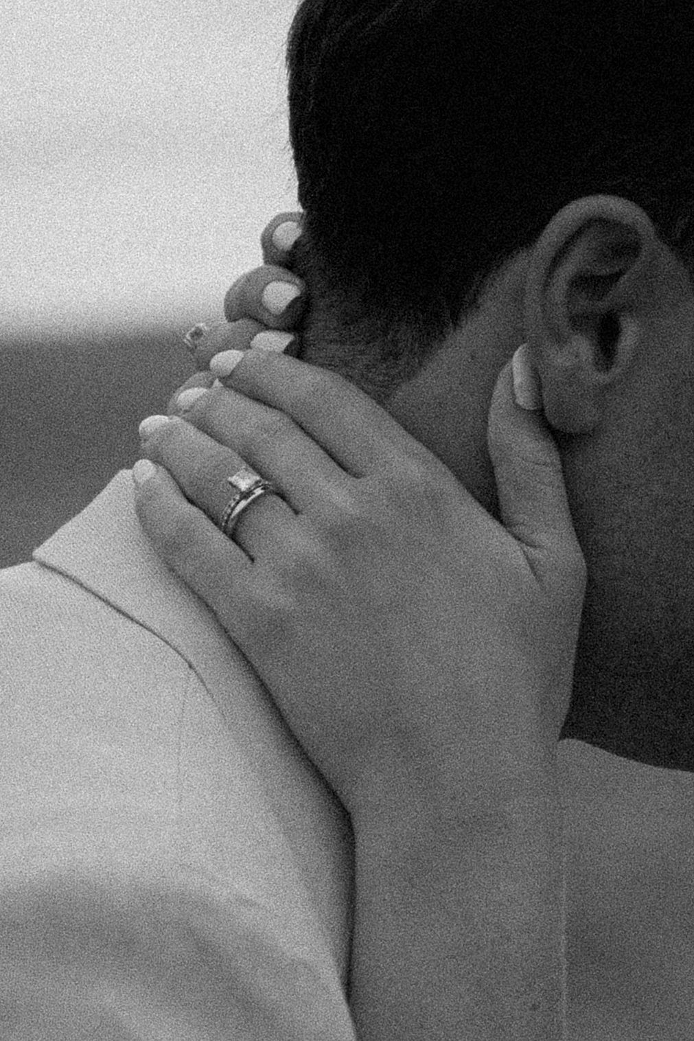 Close-up black and white photo of hands and wedding ring against neck.