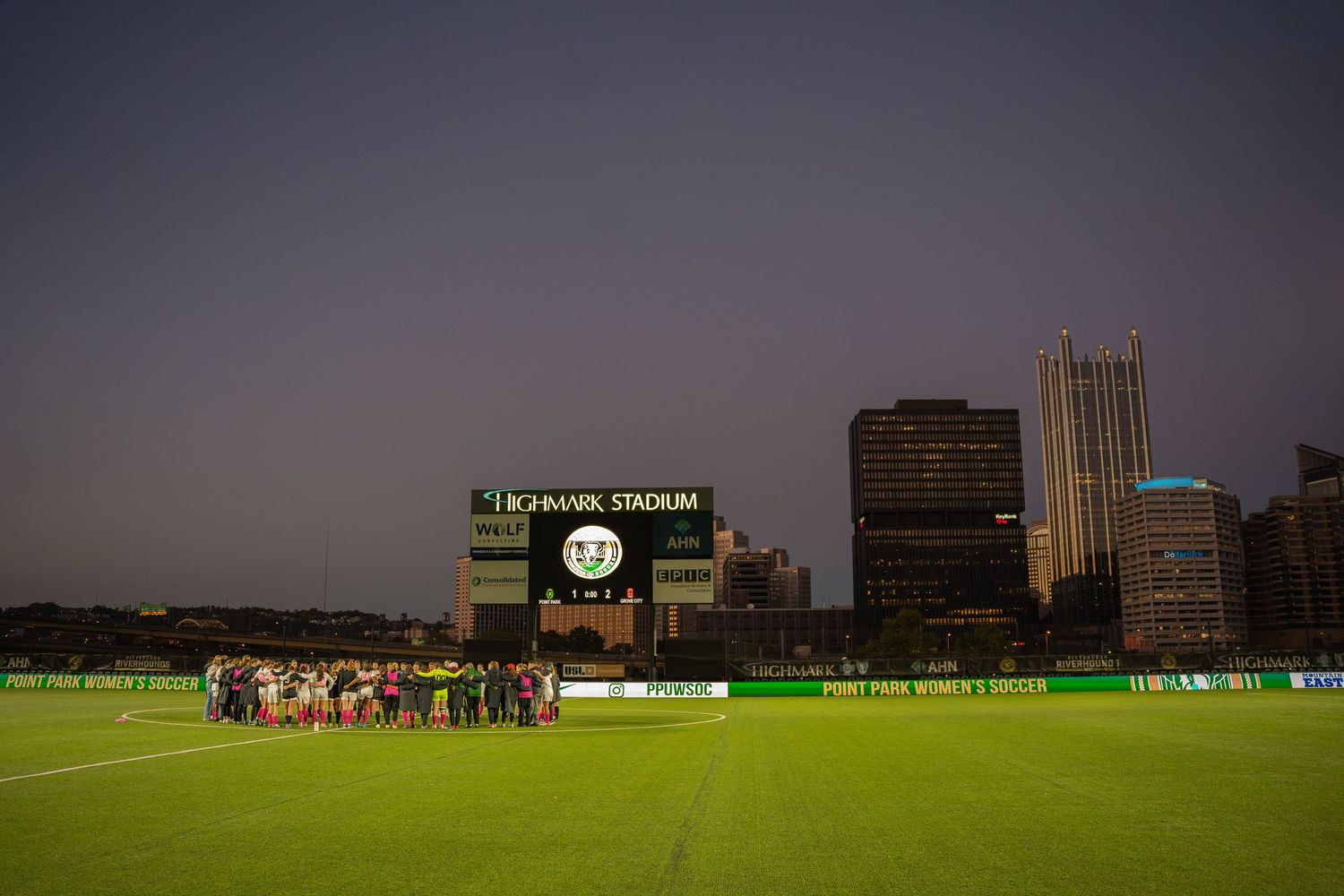 Two teams huddled together at night at Highmark Stadium in Pittsburgh