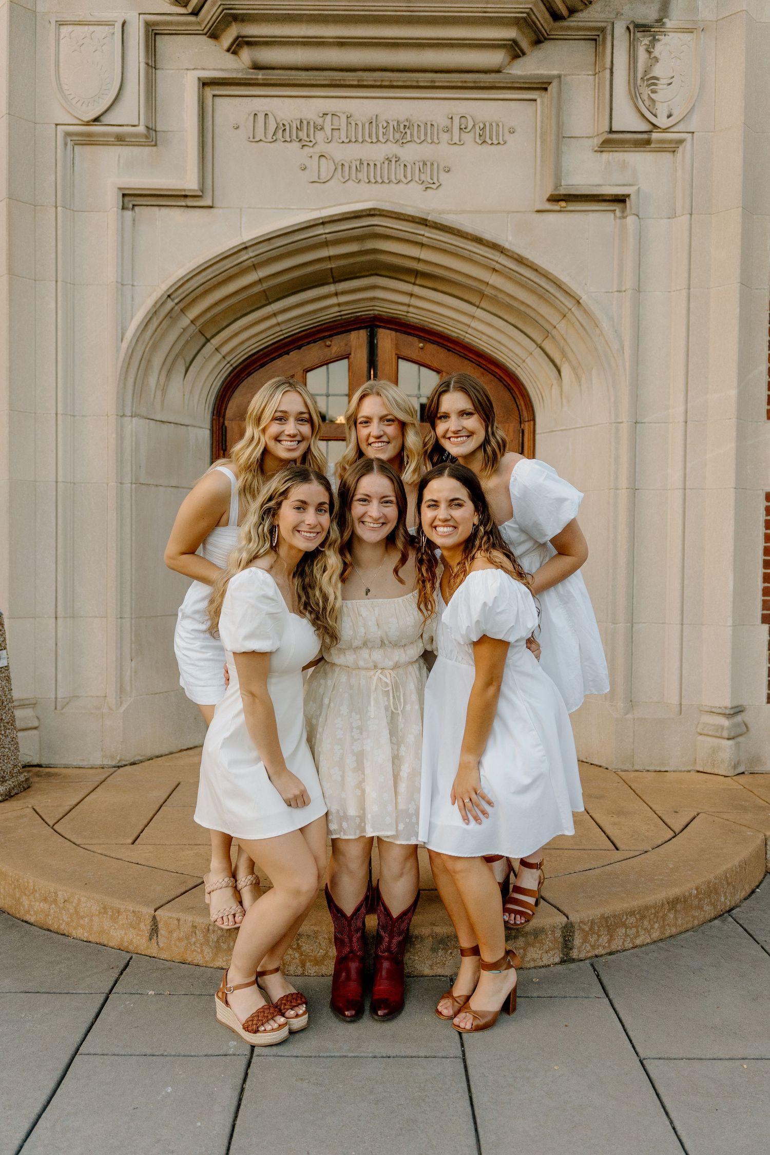Friends in white dresses pose together under ornate stone archway for group photos.