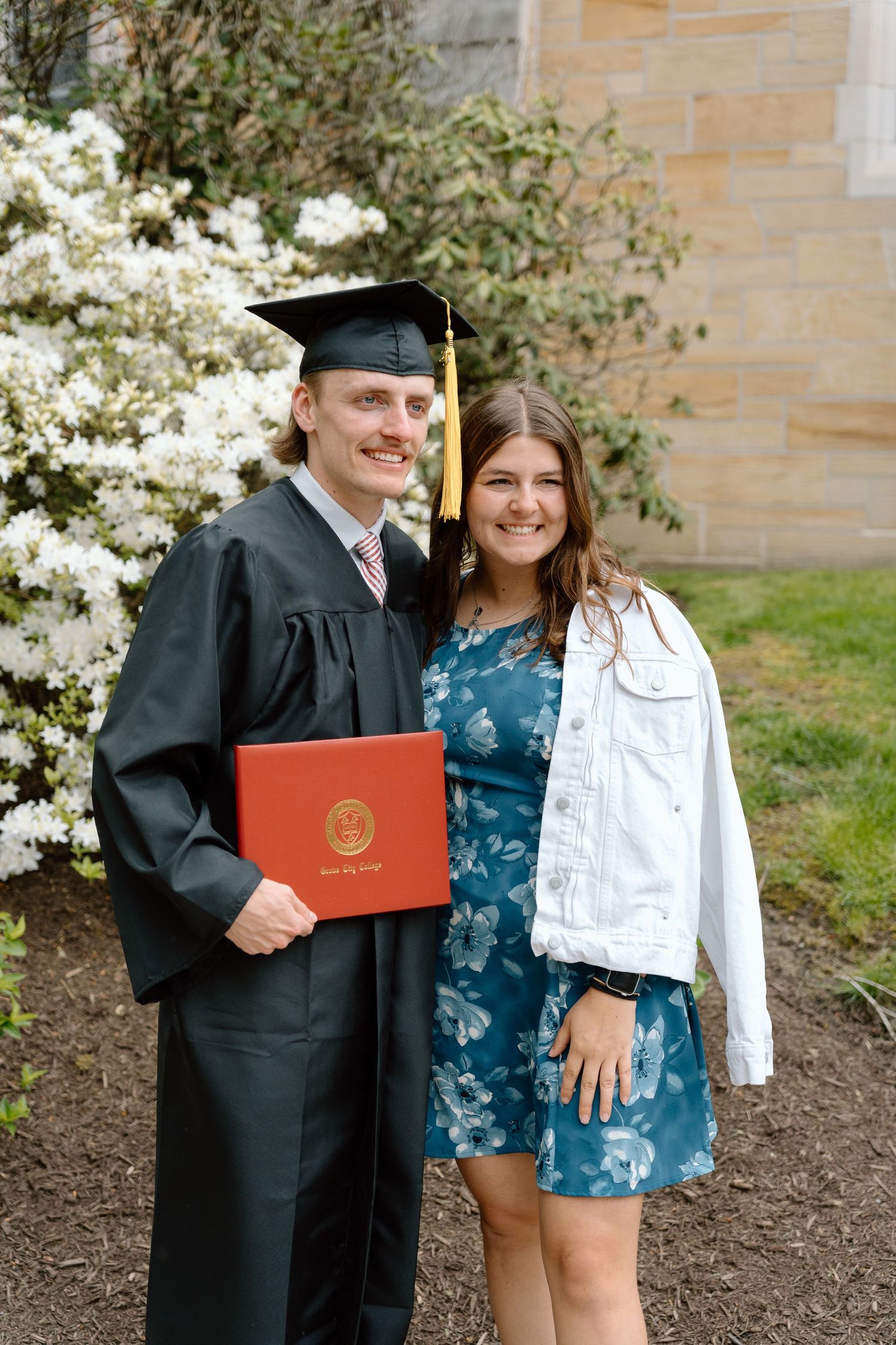 Graduate holding diploma poses with family members outside university building.