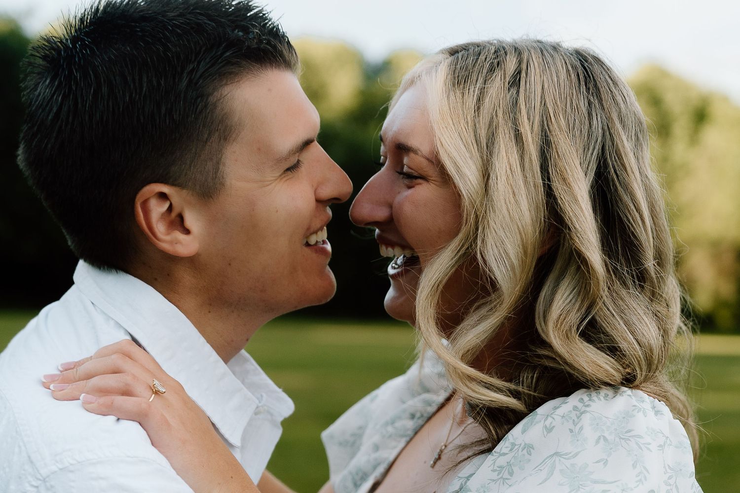 A smiling couple sharing a romantic moment outdoors, gazing at each other on a lush green background.