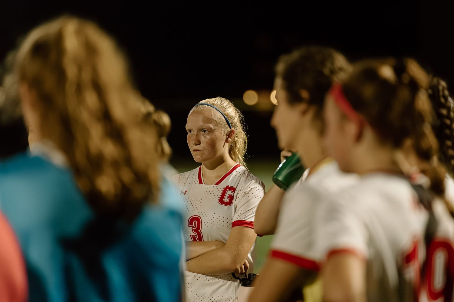 Athletes in red and white uniforms standing during nighttime sporting event.