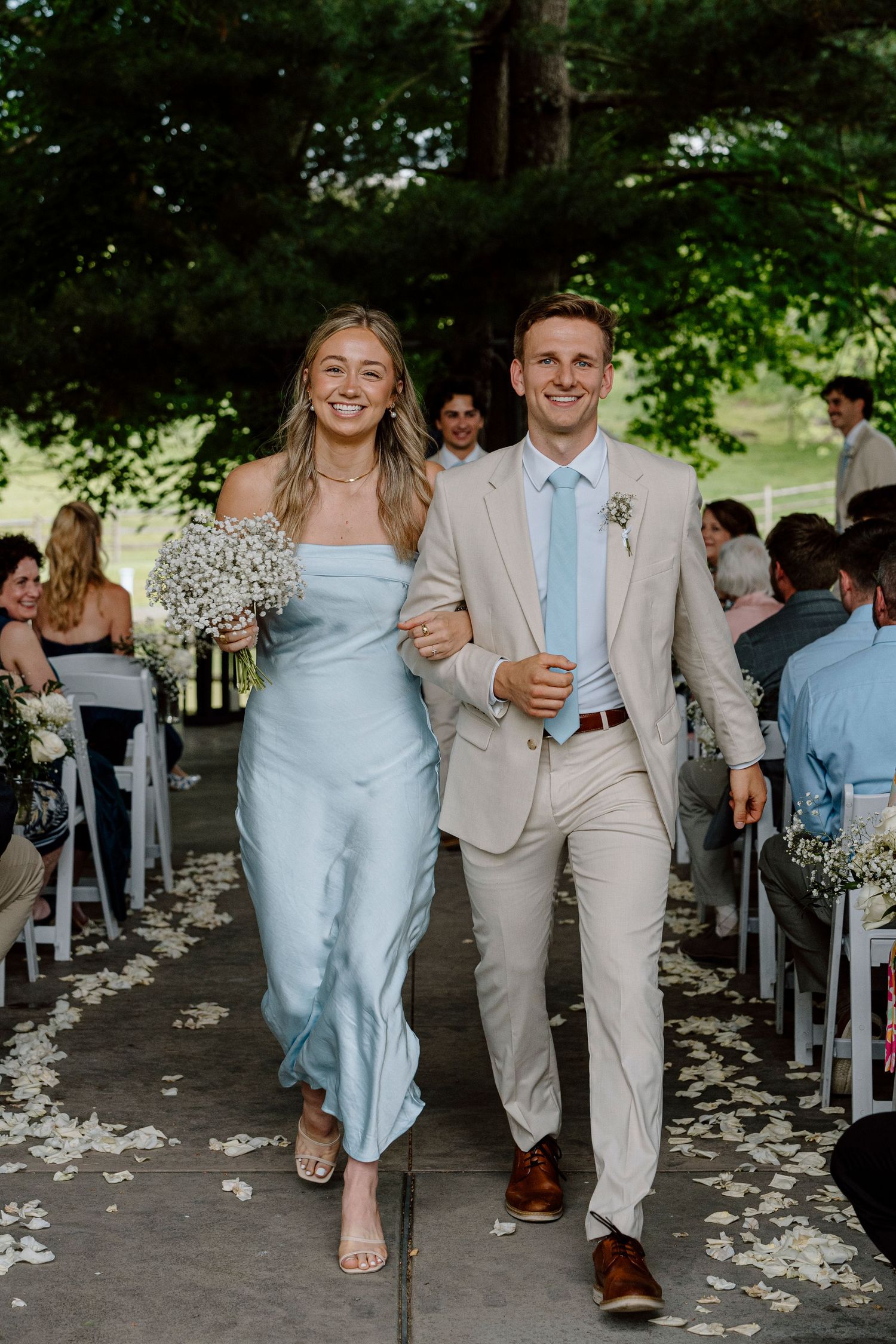 Wedding couple walking down aisle with flower petals scattered on ground.