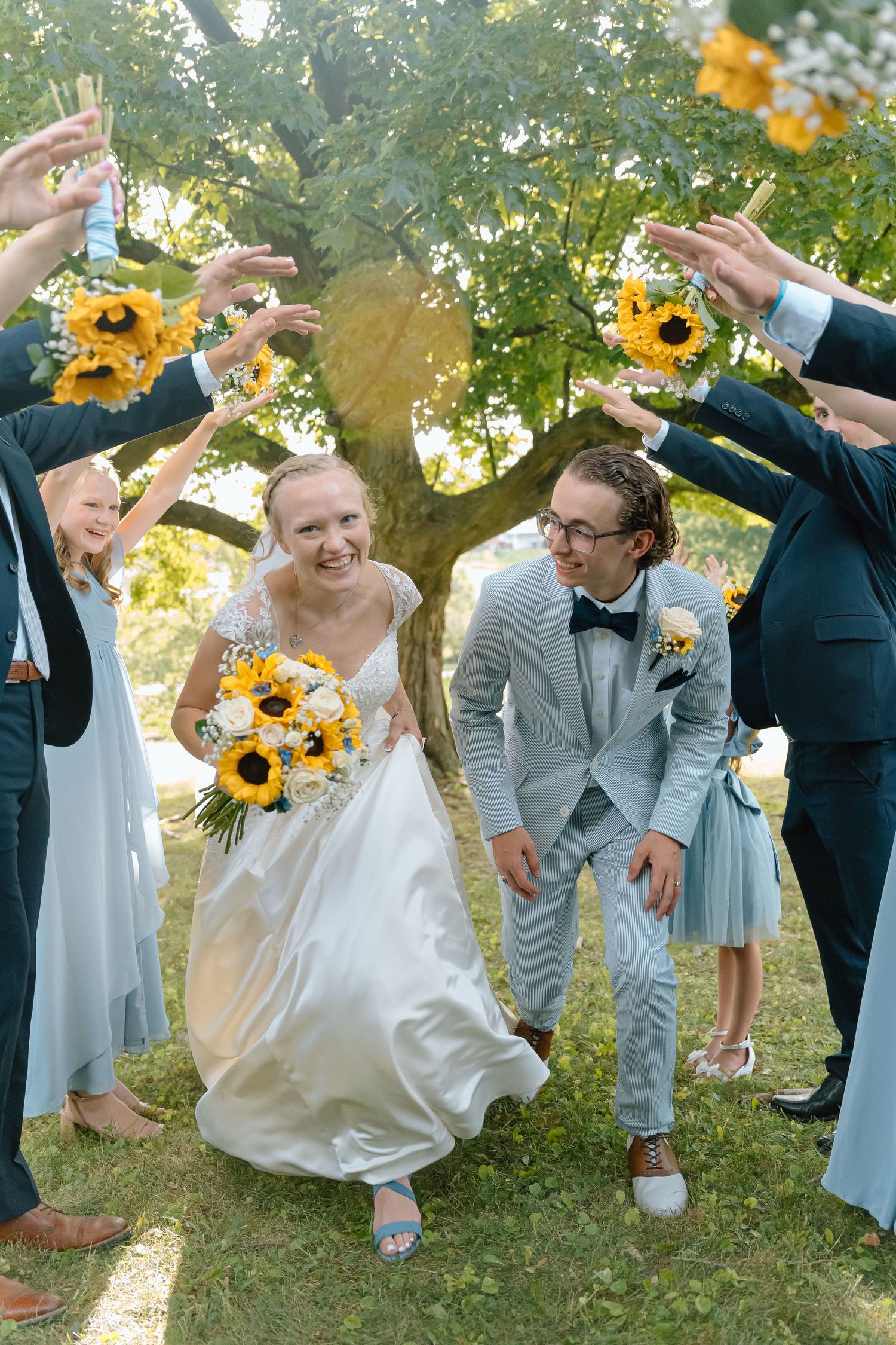 Joyful wedding party celebrates outdoors with bright sunflowers and casual style in a sunlit garden setting.