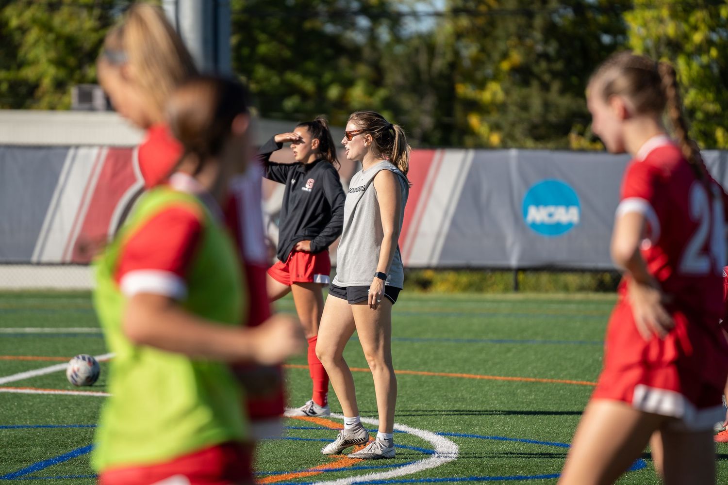 Athletes practicing on sports field with equipment visible in background.