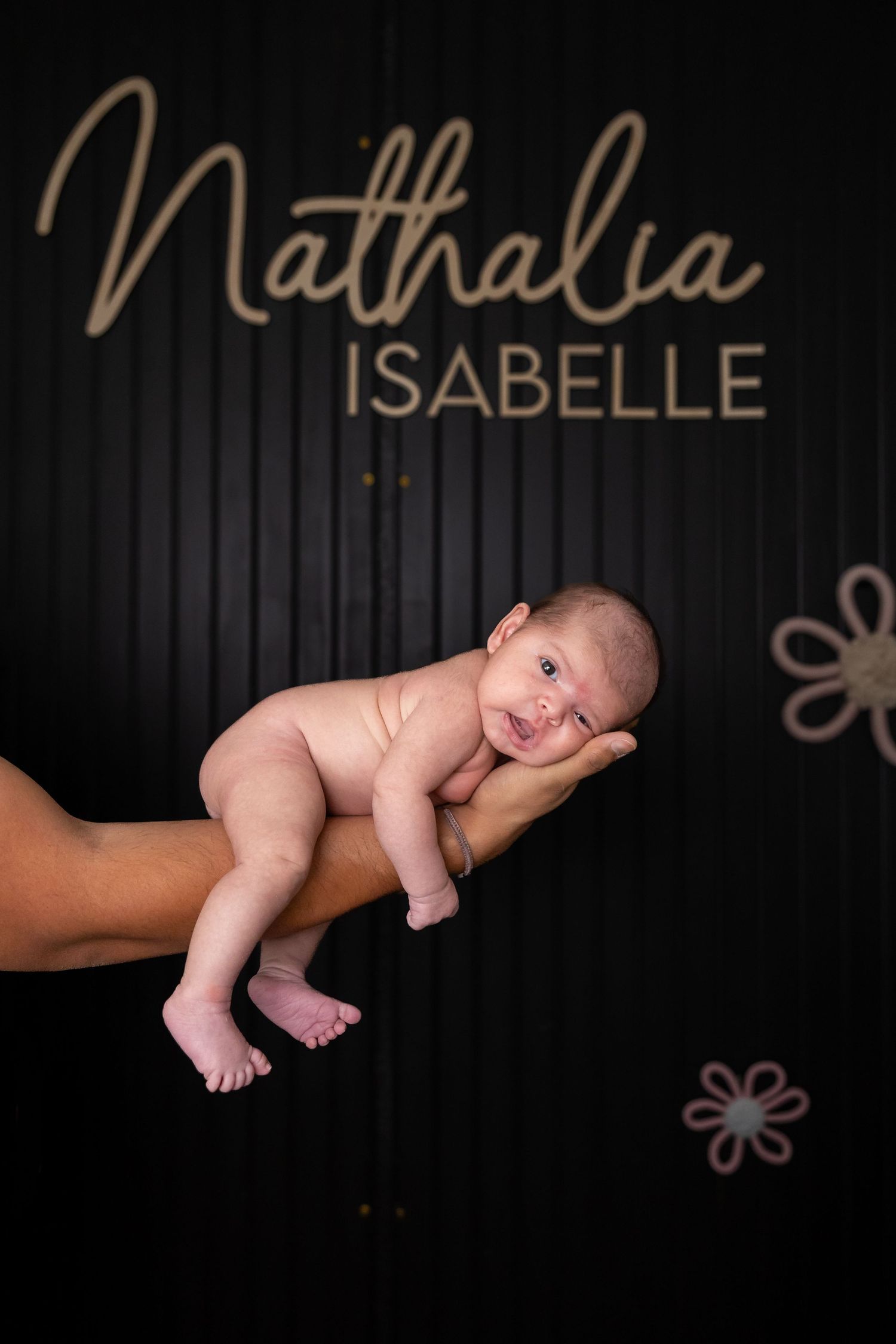Newborn baby rests gently on adult's hands against dark background with decorative name 