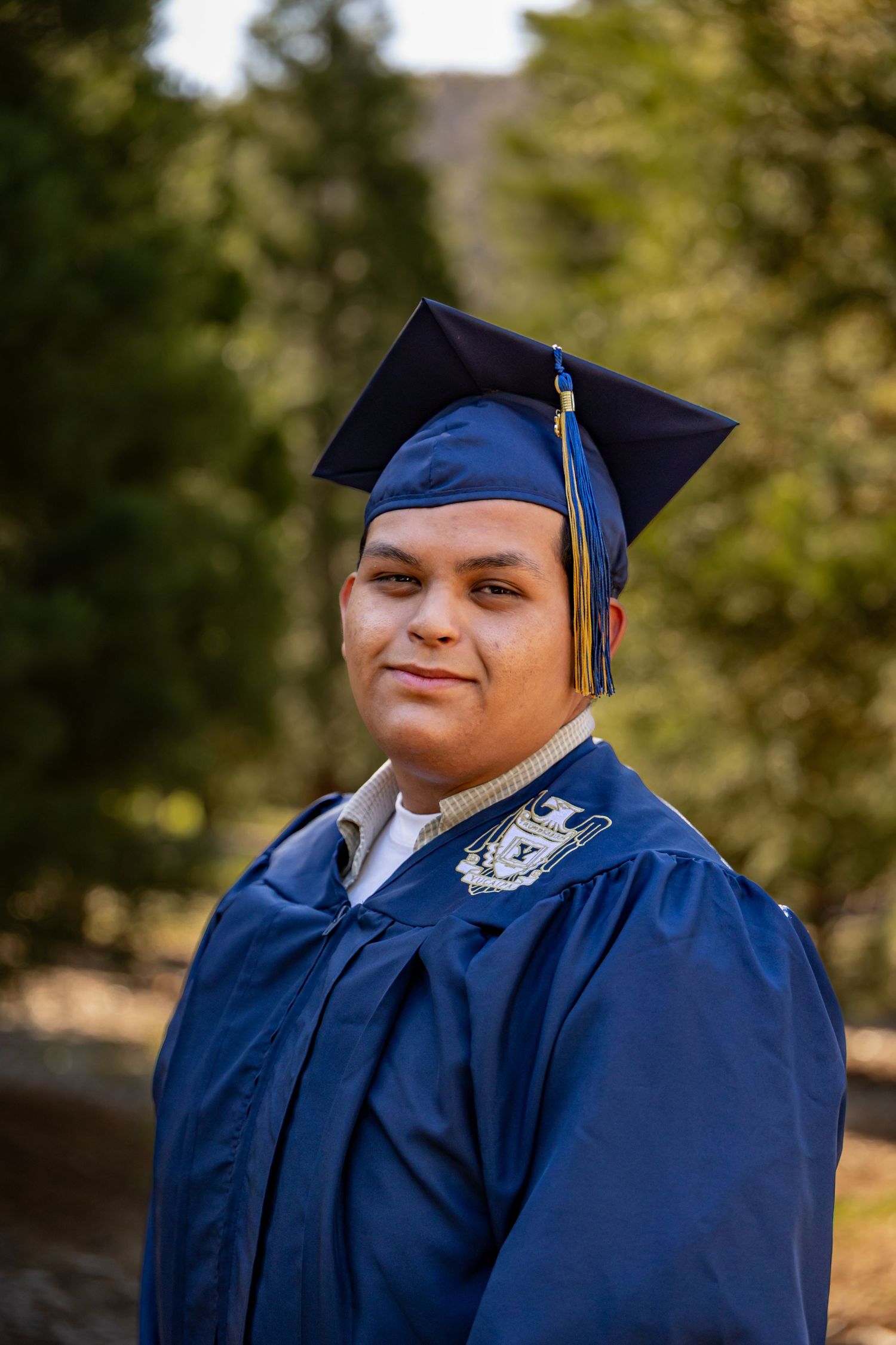 A graduate poses in traditional blue cap and gown regalia outdoors in Yucaipa.
