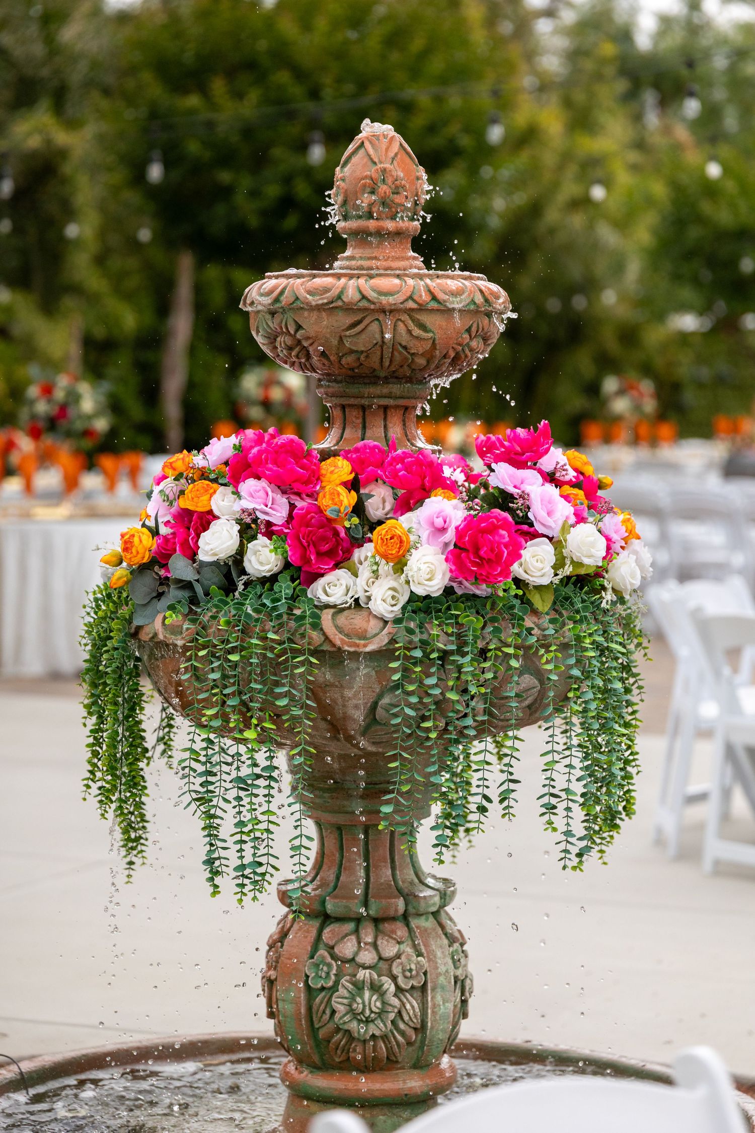 Ornate stone fountain decorated with cascading colorful flowers and trailing greenery.