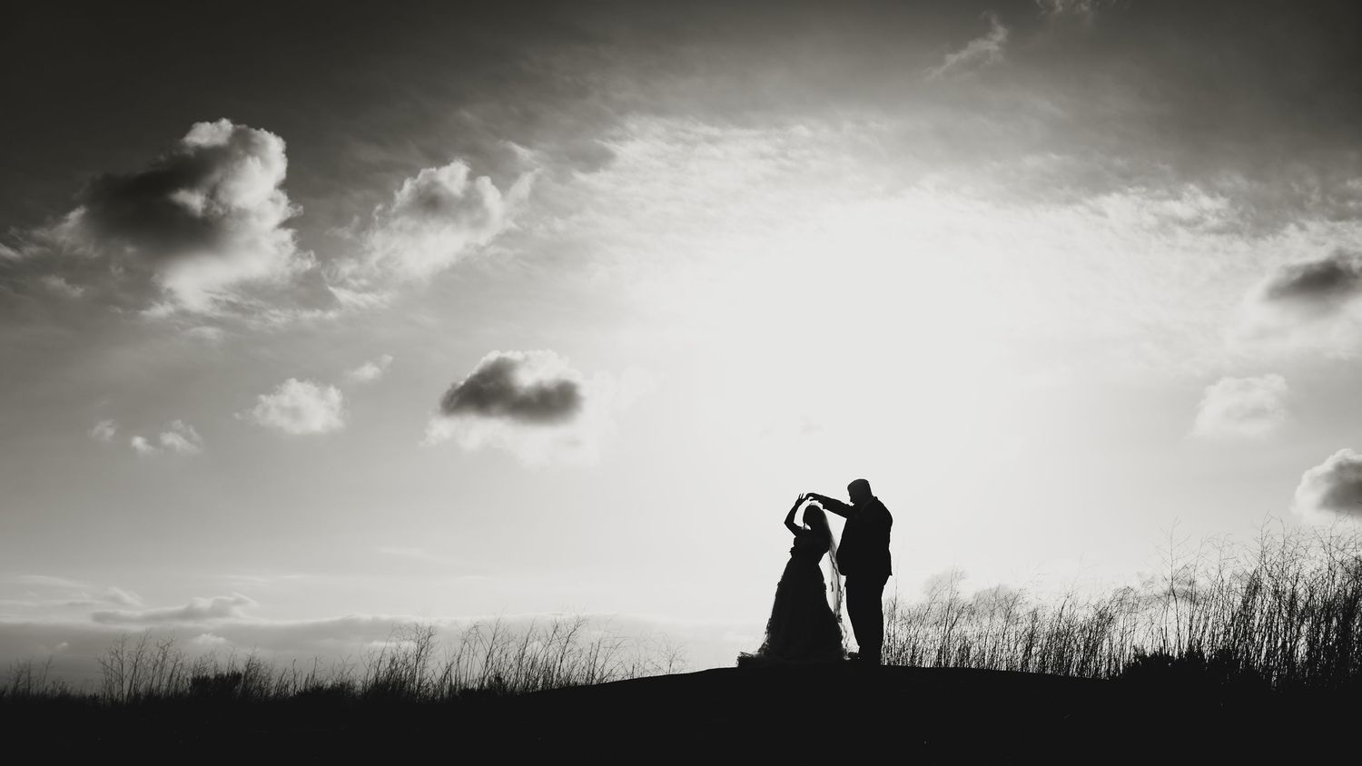 Wide black and white landscape view with dramatic clouds and silhouetted figures against the sky.