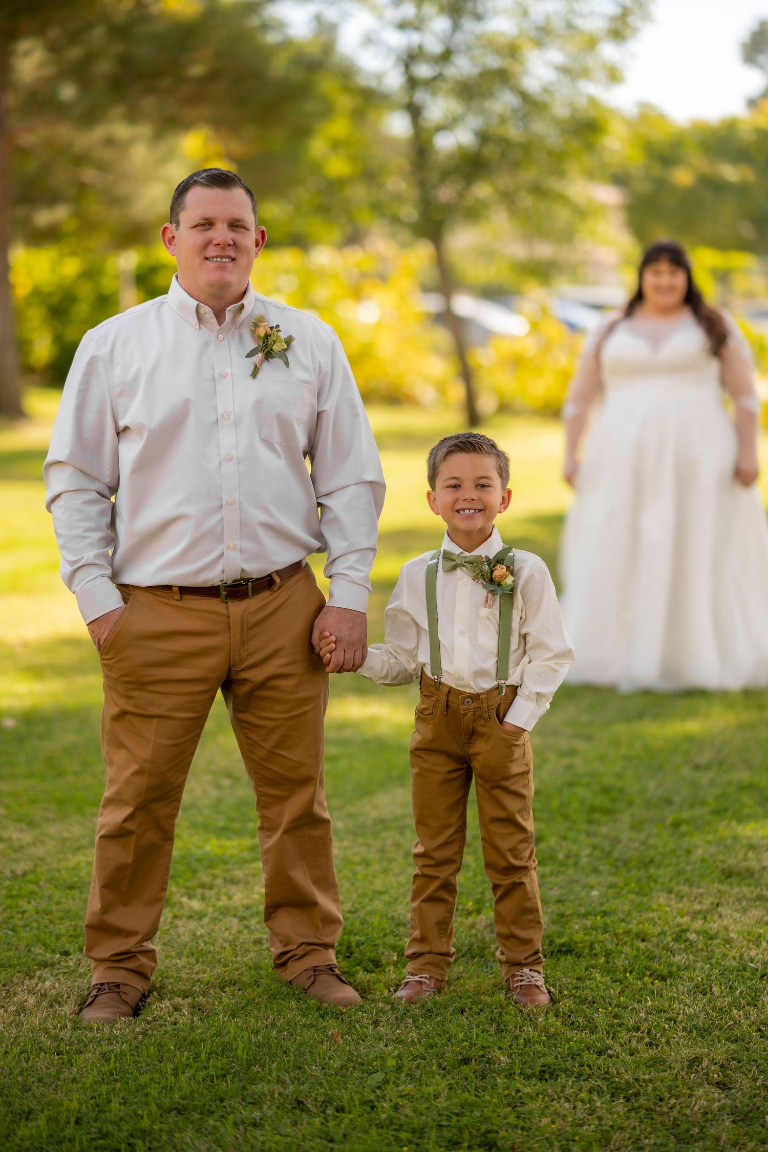 A wedding photo showing matching brown pants outfits and floral boutonnieres against a sunny outdoor backdrop.