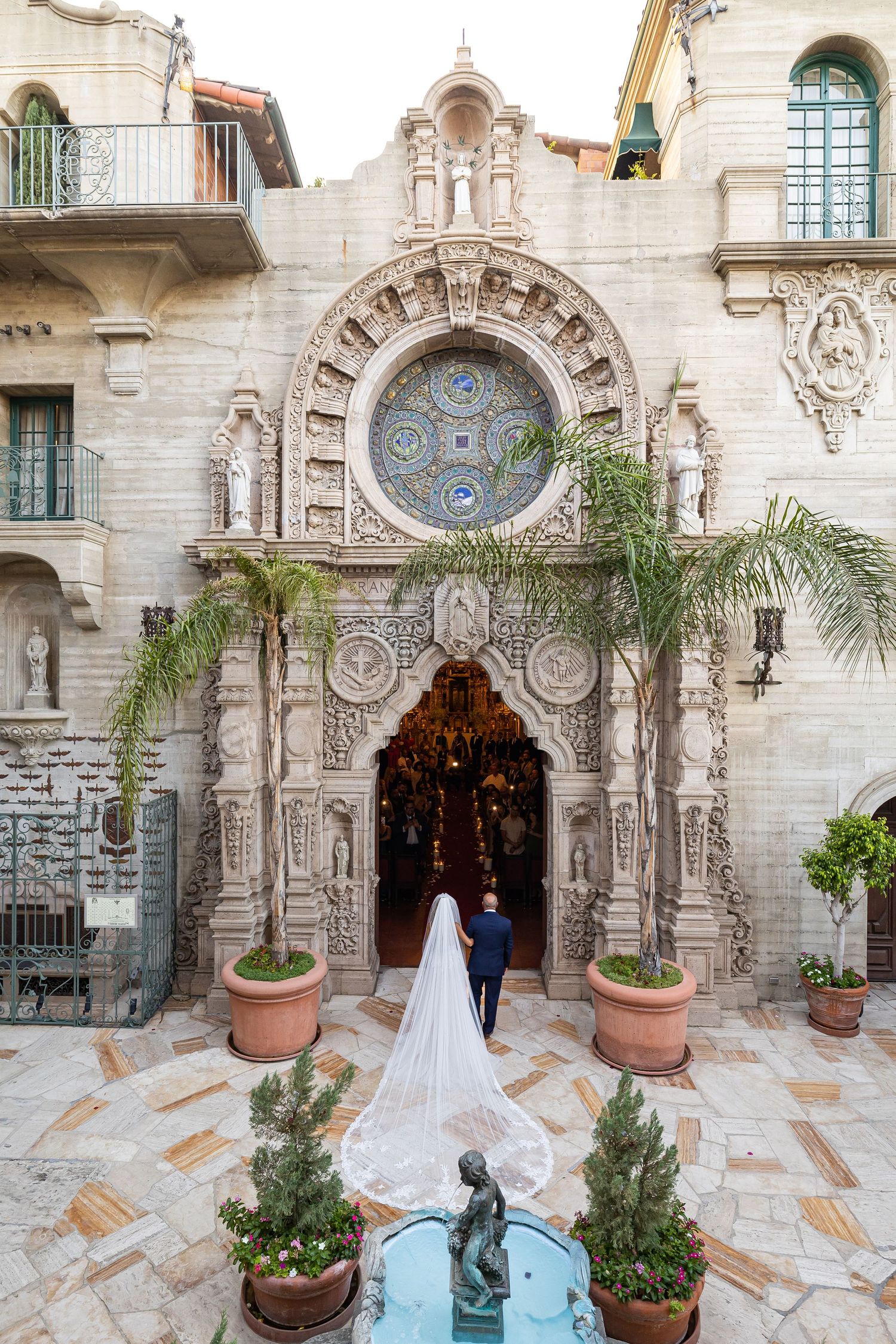 Bride and groom entering ornate church with detailed architecture and long trailing veil.