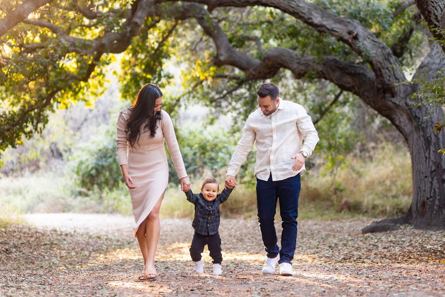 Parents walk with small child under autumn trees on nature path.
