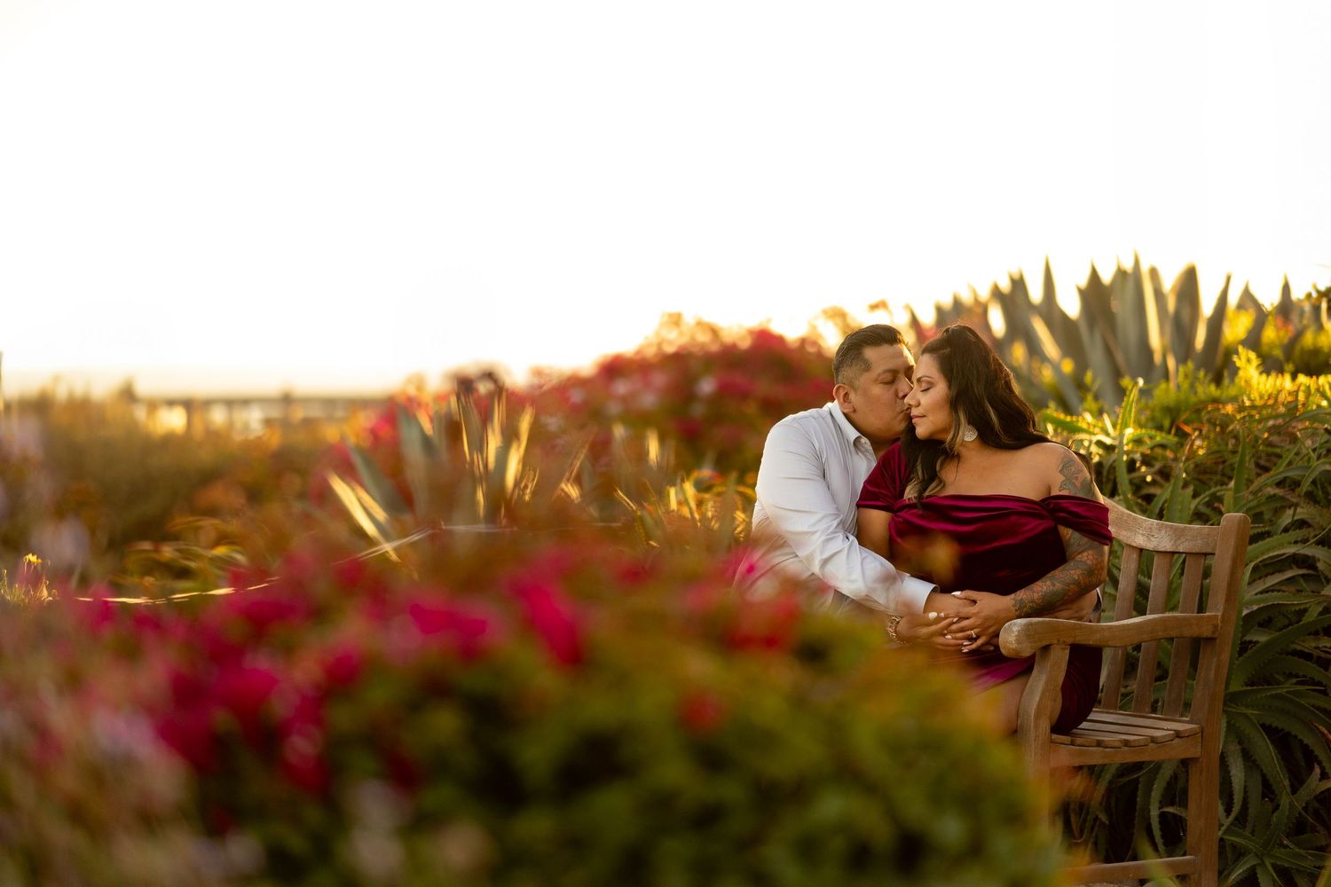 A wooden table outdoors decorated with floral centerpieces and place settings at sunset against mountain scenery.