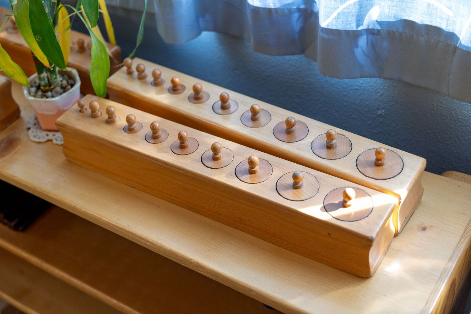 A wooden Montessori cylinder block with graduated size knobs sitting on a light-colored table.