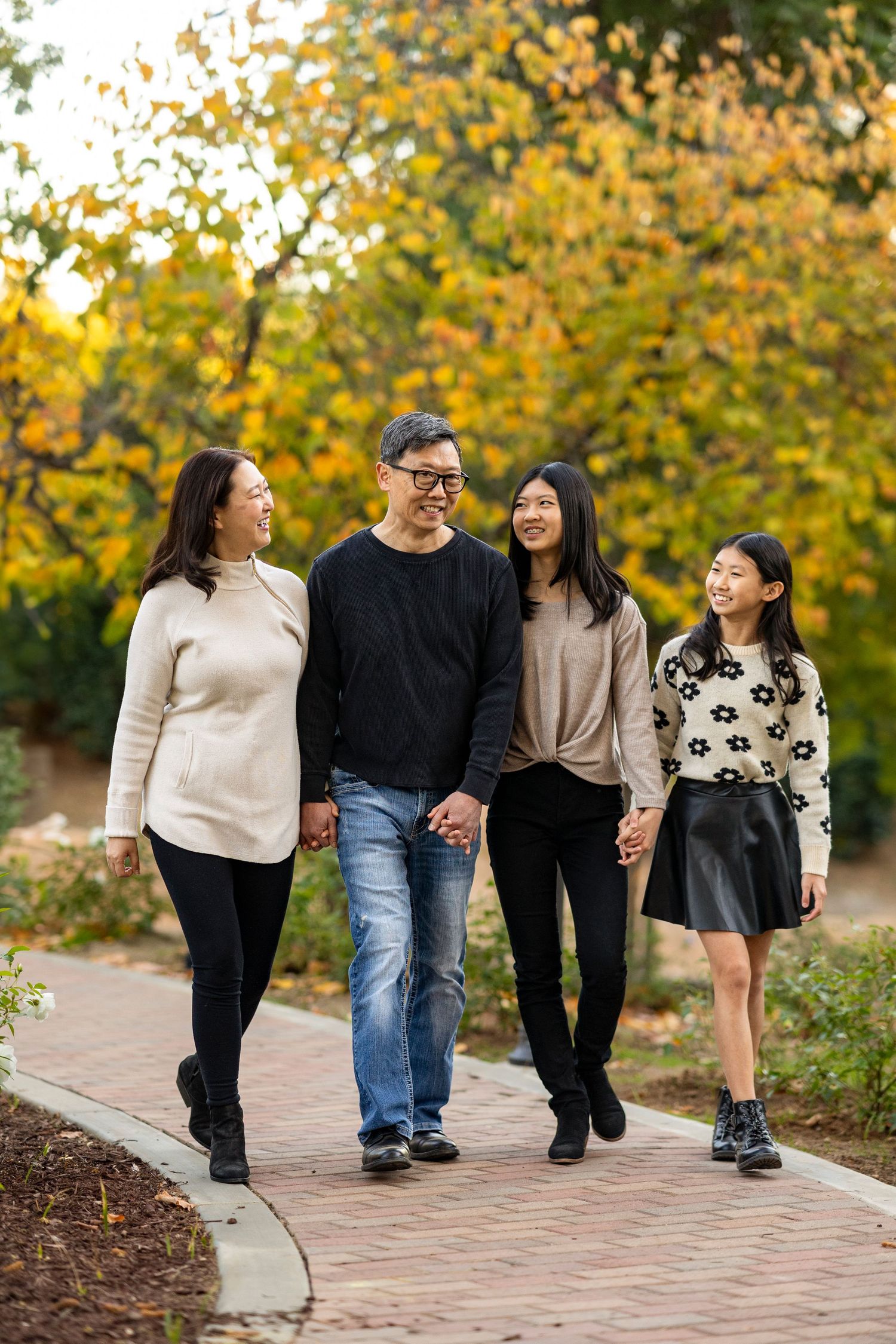 Family of four walks together on brick pathway surrounded by fall foliage.