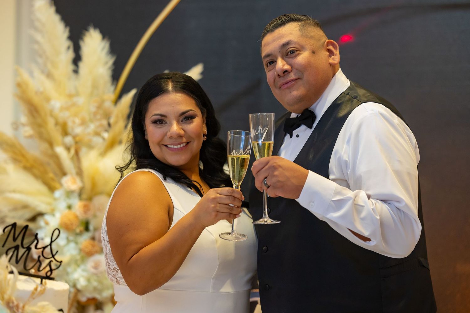 Wedding couple toasting with champagne glasses beside pampas grass decor.