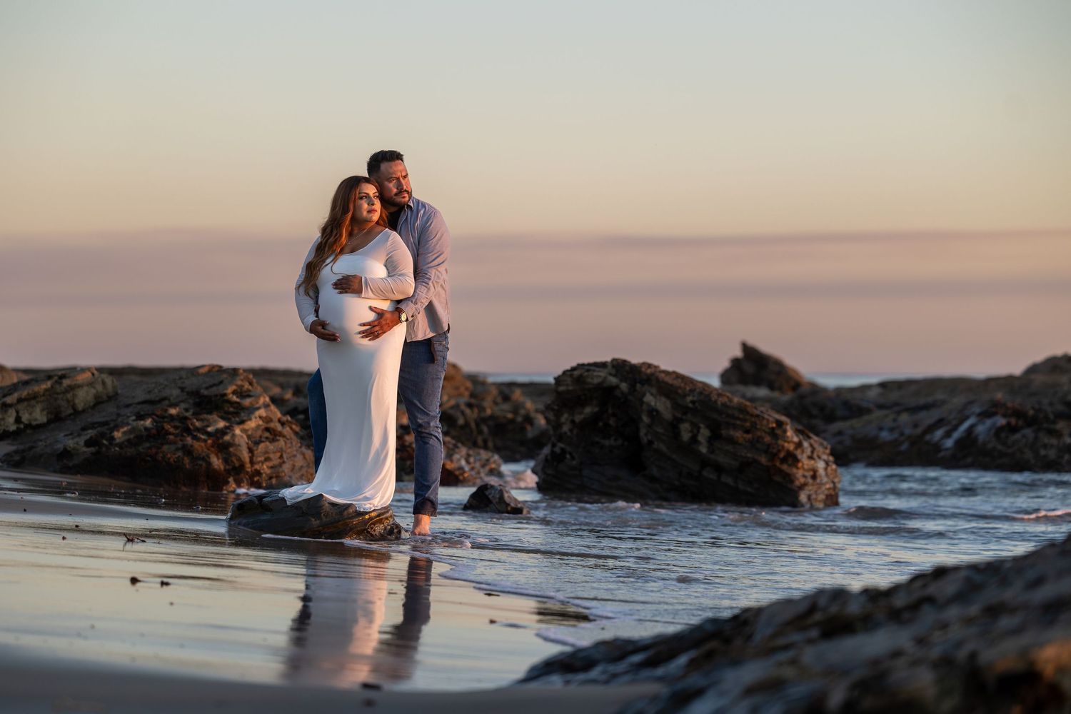 Couple embracing on rocky beach during sunset in Huntington Beach.