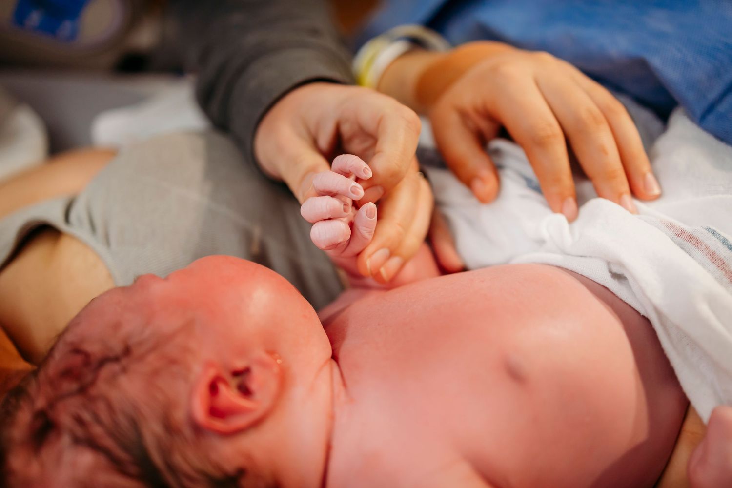 Tiny newborn baby being examined by medical hands shortly after birth while crying.