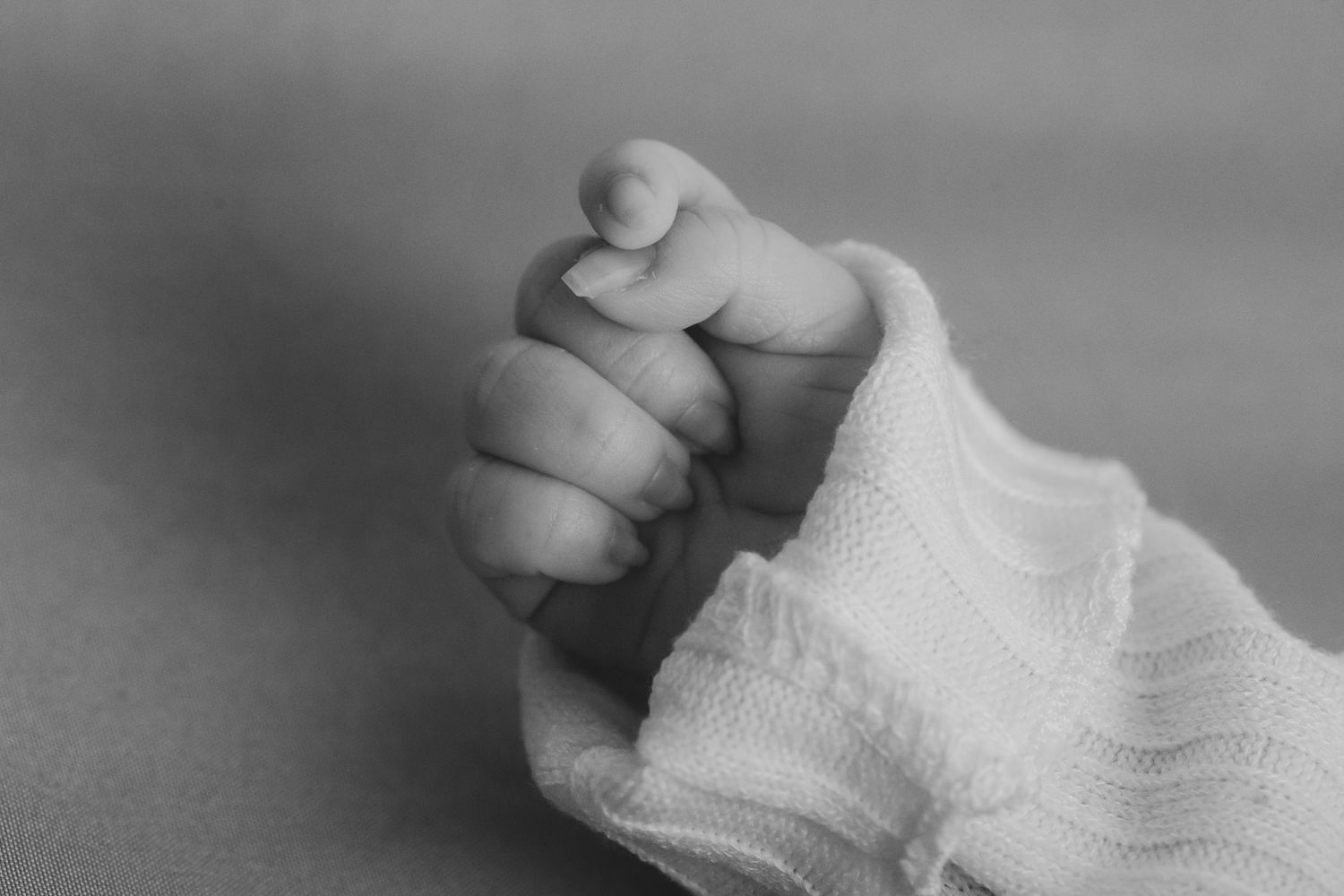A tiny newborn baby's hand grasps tightly onto a finger in this intimate black and white photograph.