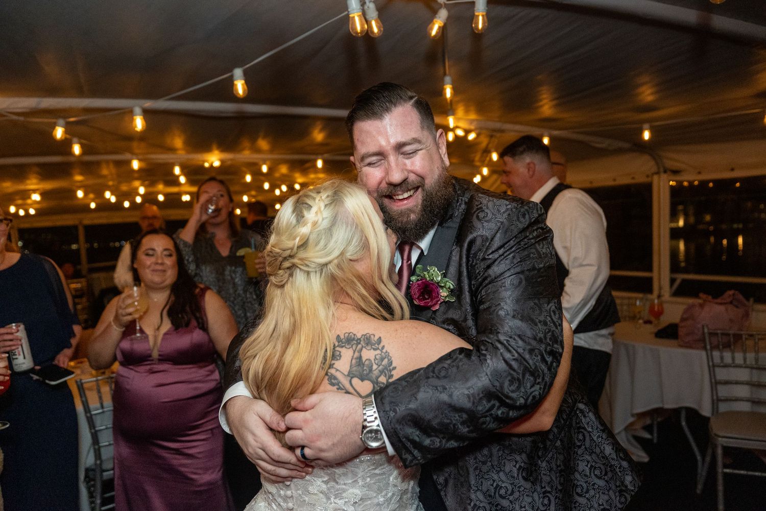 Couple sharing joyful dance moment at wedding reception under string lights.