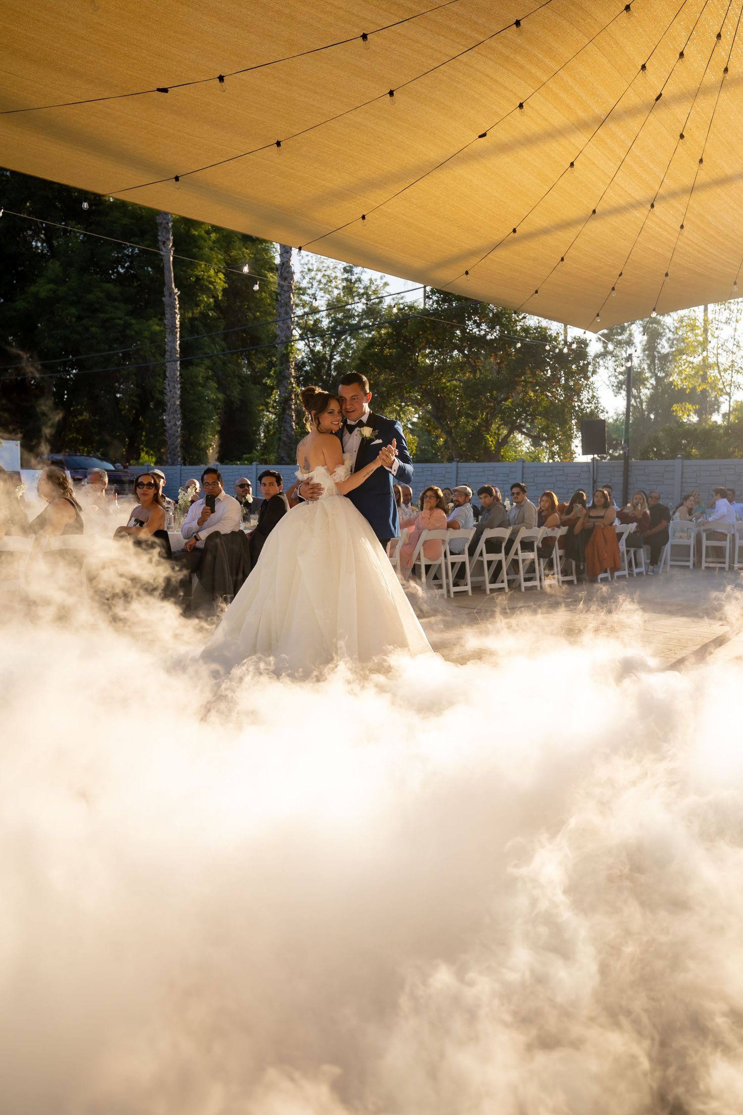 Dramatic fog effect creates atmosphere during an outdoor wedding reception under string lights.