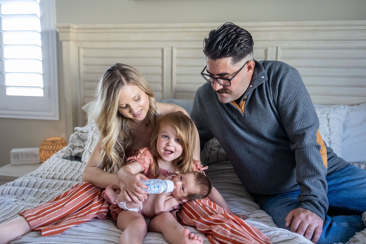 Family sharing an intimate moment together on a cozy bed with grey bedding.