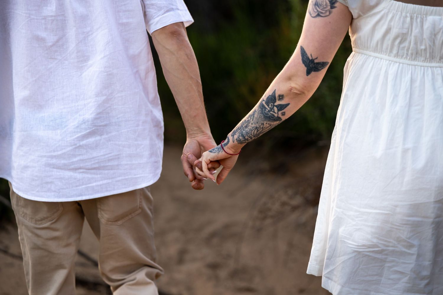 Close-up of tattooed hands holding each other against white and beige clothing.