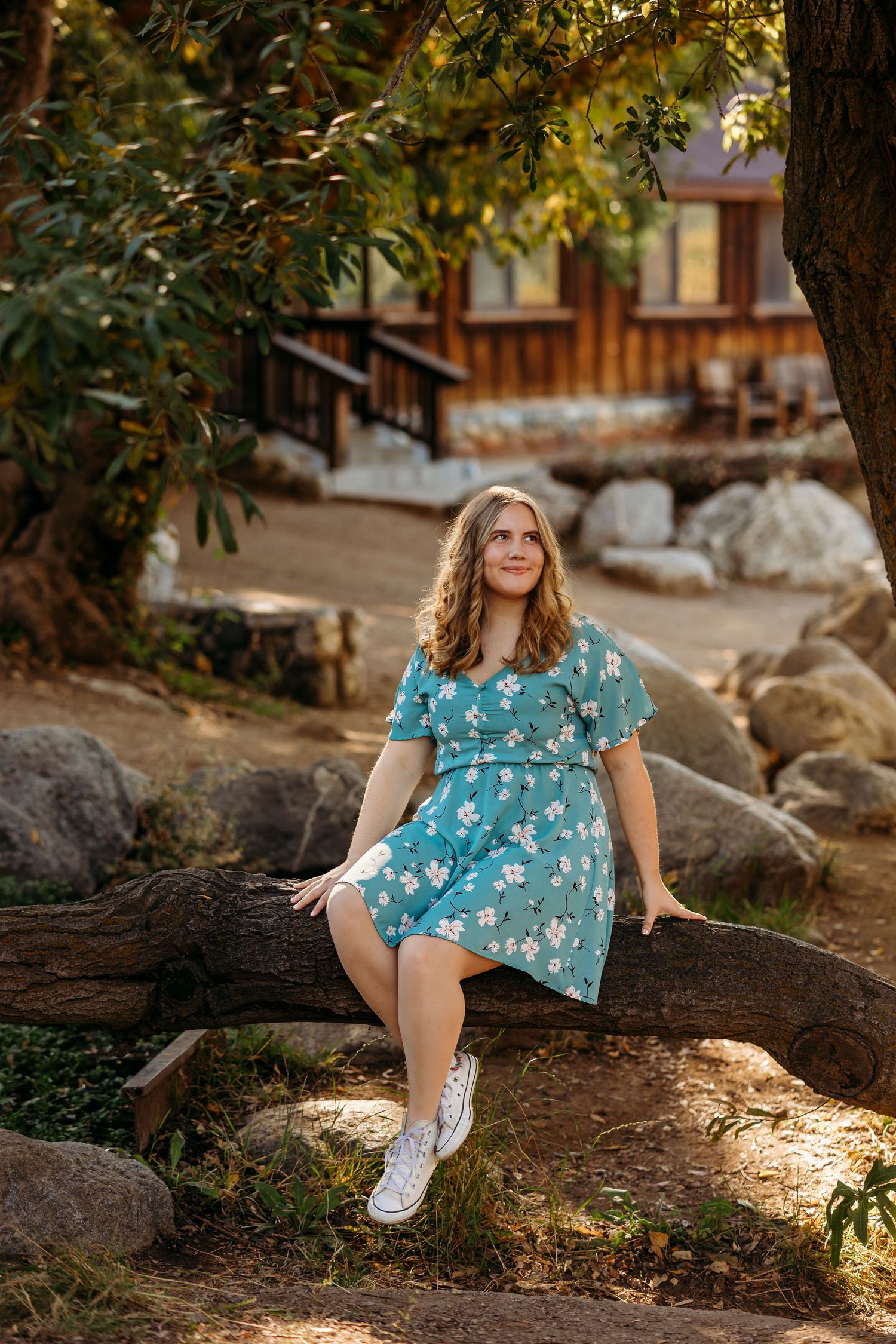 A floral blue dress and white sneakers complement this casual outdoor photoshoot on a fallen log in Oak Glen.