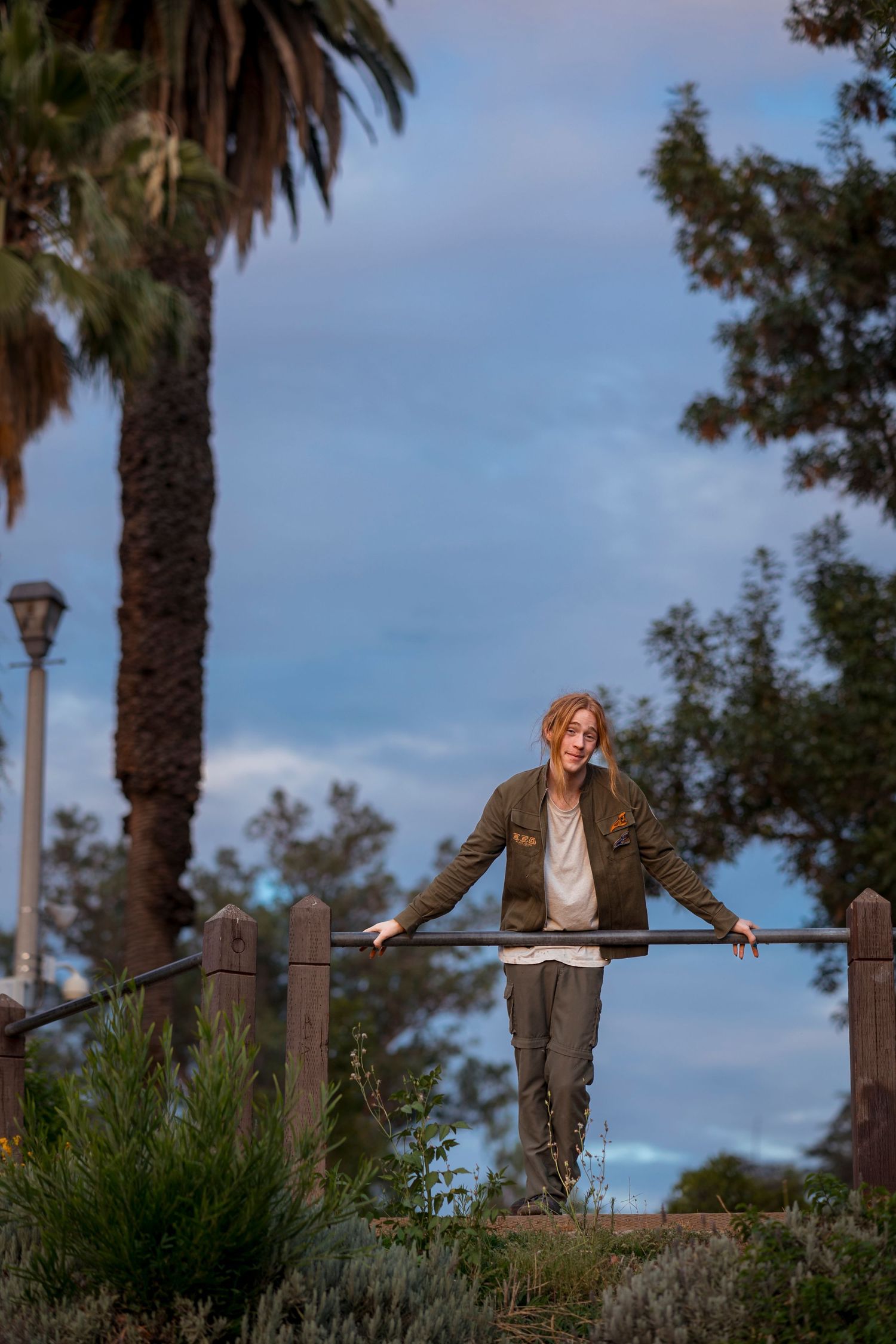Evening sky with palm trees frames Graduate leaning on railing at dusk in Redlands.