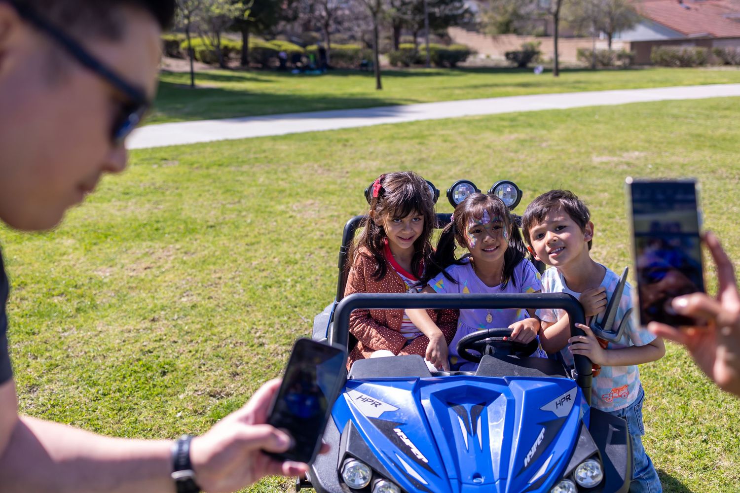 Group taking selfies around a blue ATV on a grassy hill.