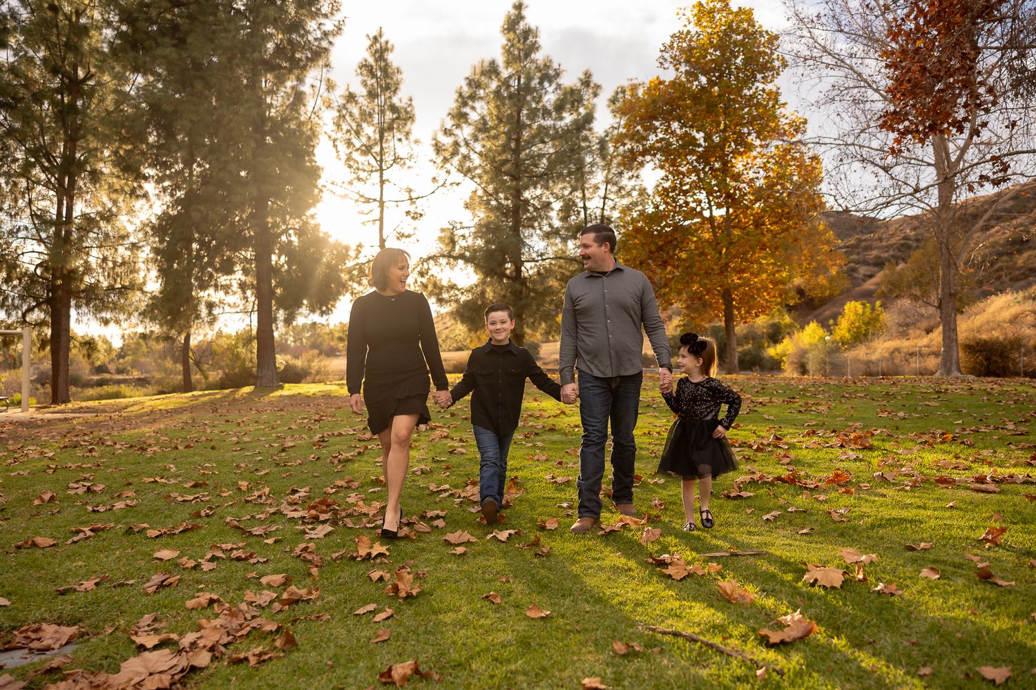 Family members walk together on a grassy hill during golden hour sunset.