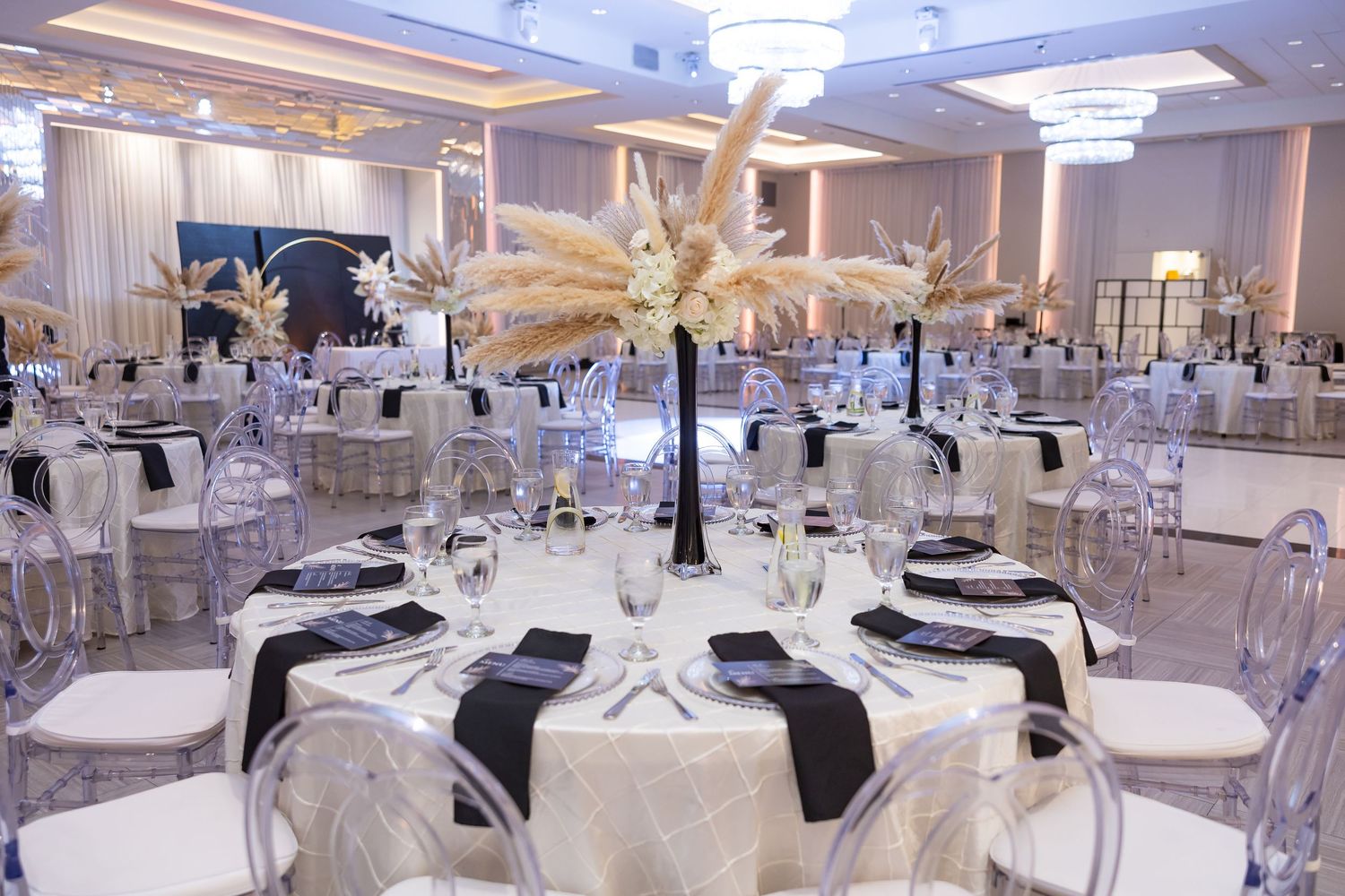 Elegant wedding reception ballroom with crystal chandeliers and dramatic gold palm centerpieces on round tables.
